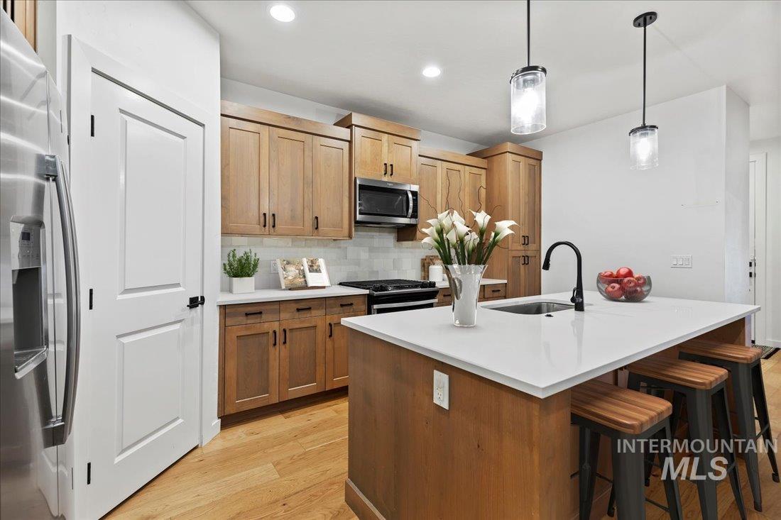 Kitchen featuring tasteful backsplash, hanging light fixtures, light wood finished floors, appliances with stainless steel finishes, and a breakfast bar