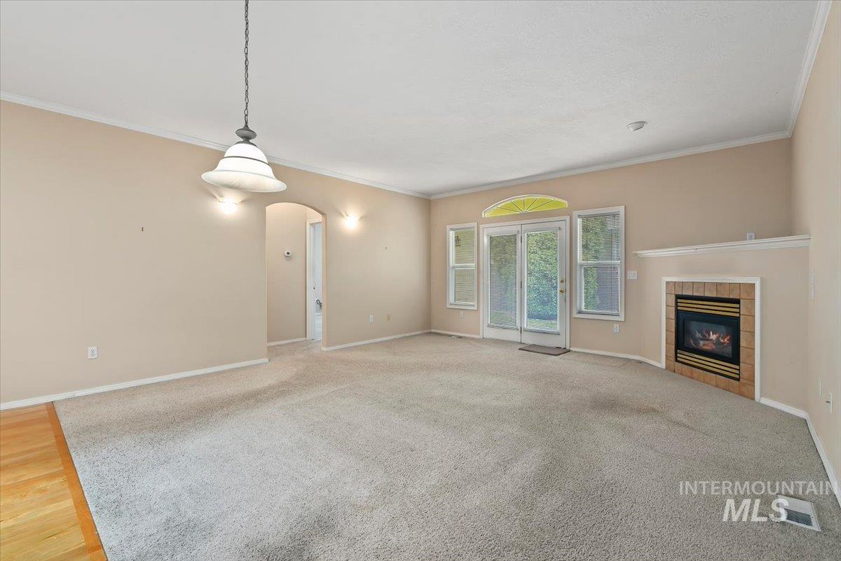 Unfurnished living room with arched walkways, a fireplace, crown molding, and light carpet