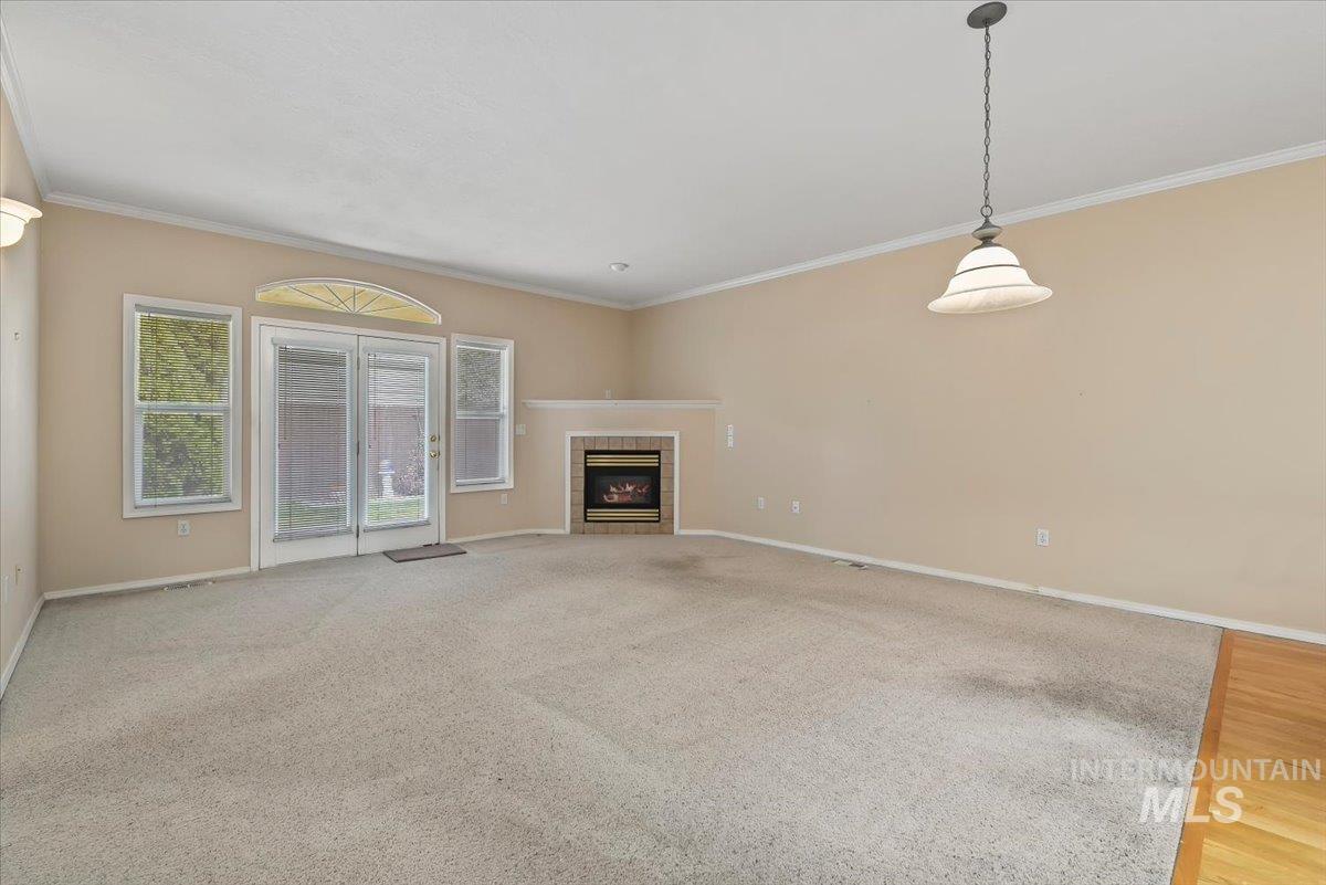 Unfurnished living room featuring a tiled fireplace, ornamental molding, and light colored carpet