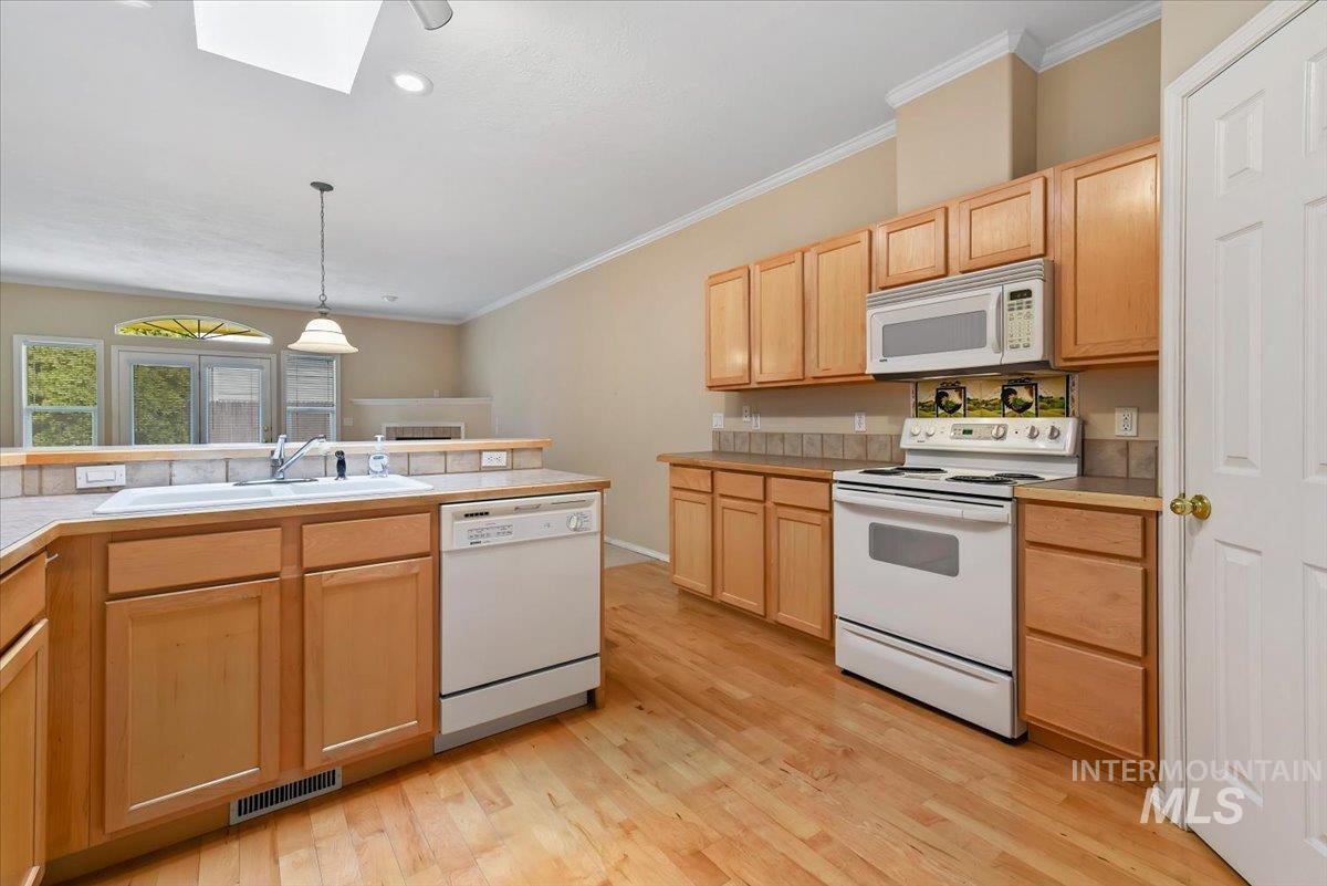 Kitchen featuring white appliances, light wood finish cabinets, light wood finished floors, ornamental molding, and pendant lighting