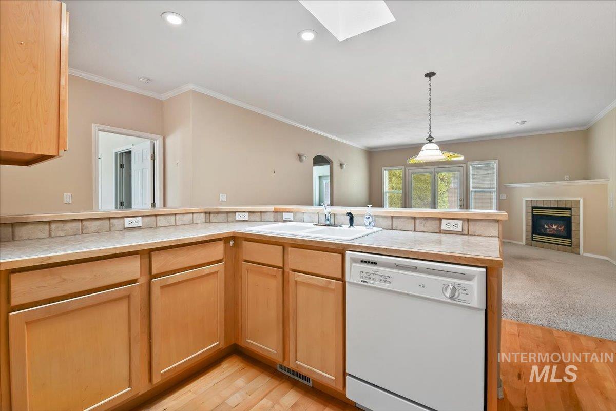 Kitchen with open floor plan, white dishwasher, a skylight, light countertops, and light wood-style flooring