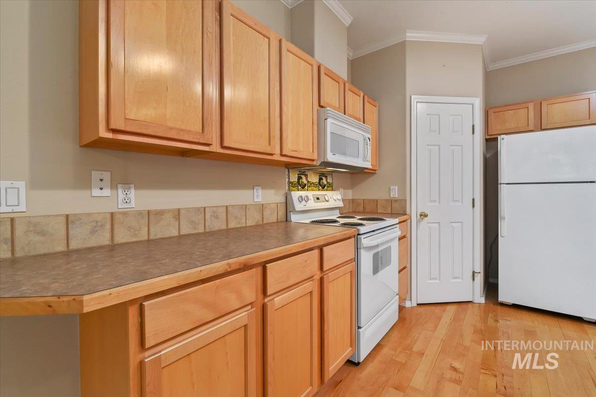 Kitchen featuring white appliances, light wood finish cabinetry, light wood-style flooring, and crown molding