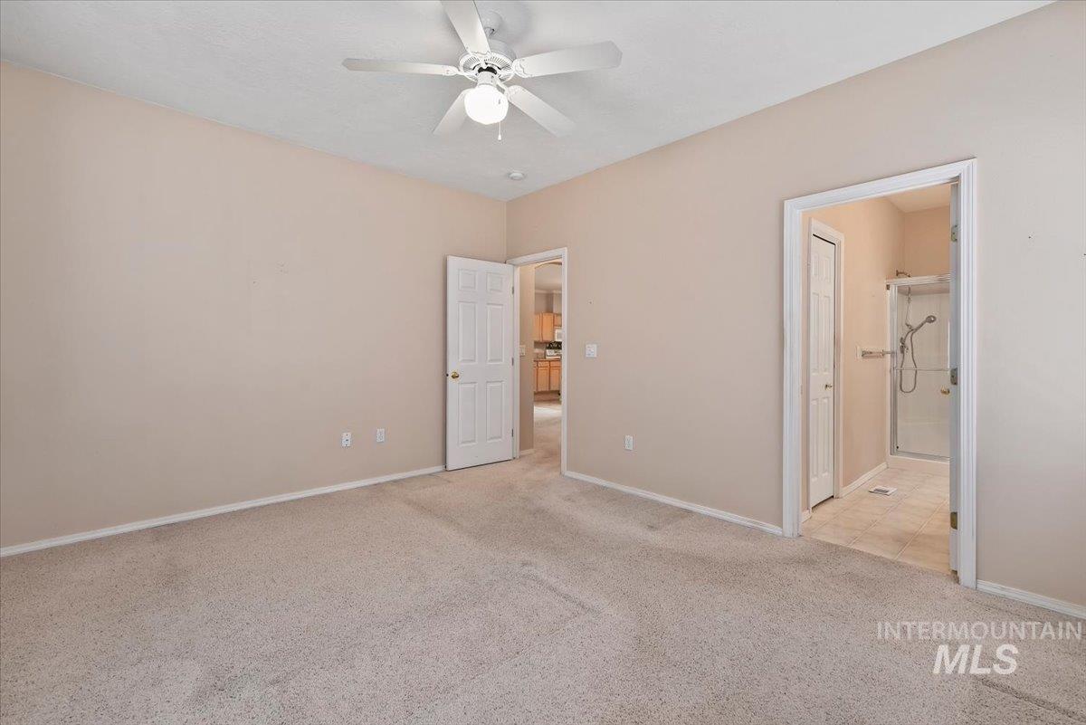 Unfurnished bedroom with light carpet, a ceiling fan, and connected bathroom