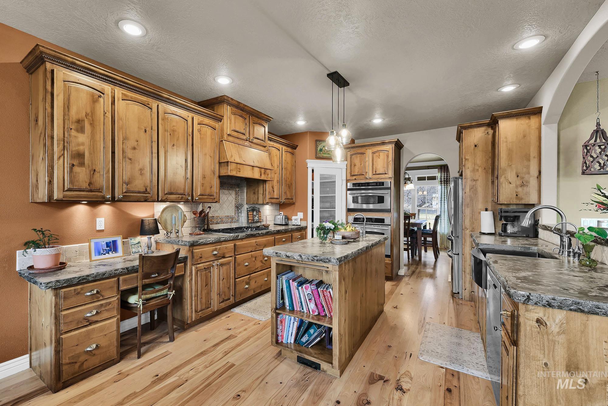 Kitchen featuring arched walkways, pendant lighting, a kitchen island, and wood finish cabinetry