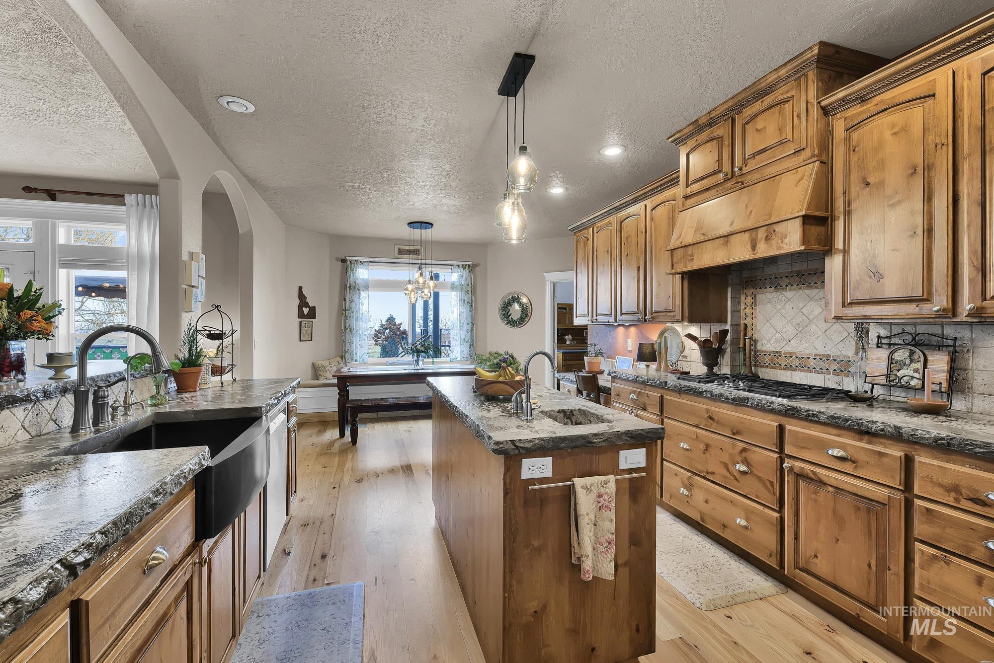 Kitchen featuring an island with sink, rustic Alder  cabinetry, pendant lighting, tasteful tile backsplash and light Maple flooring