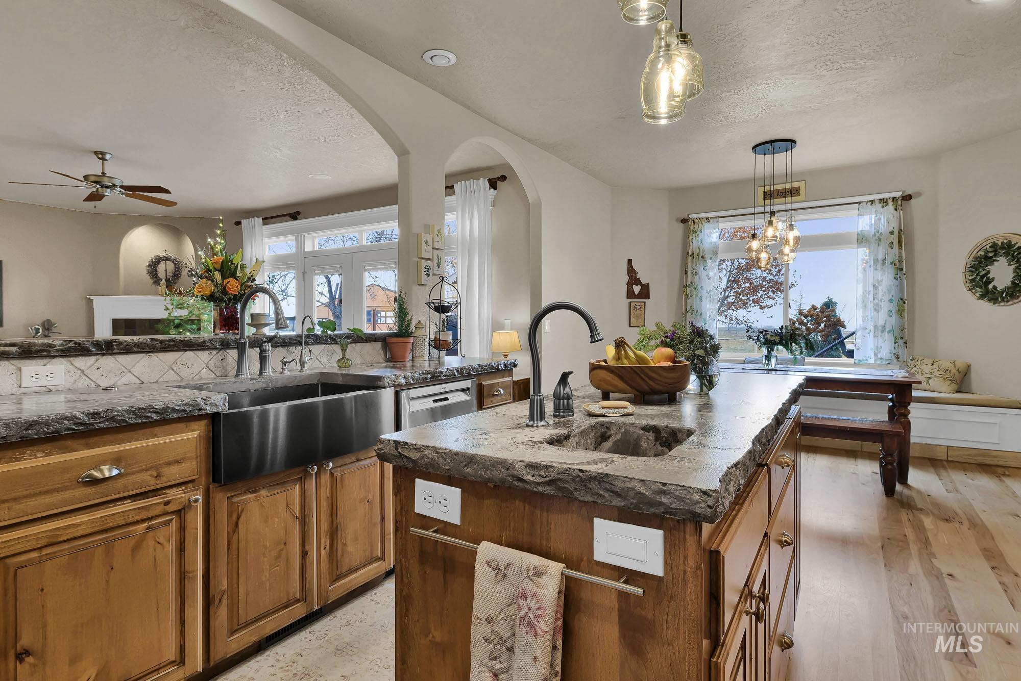 Kitchen featuring wood finish cabinetry, dark stone counters, a textured ceiling, an island with sink, and decorative light fixtures