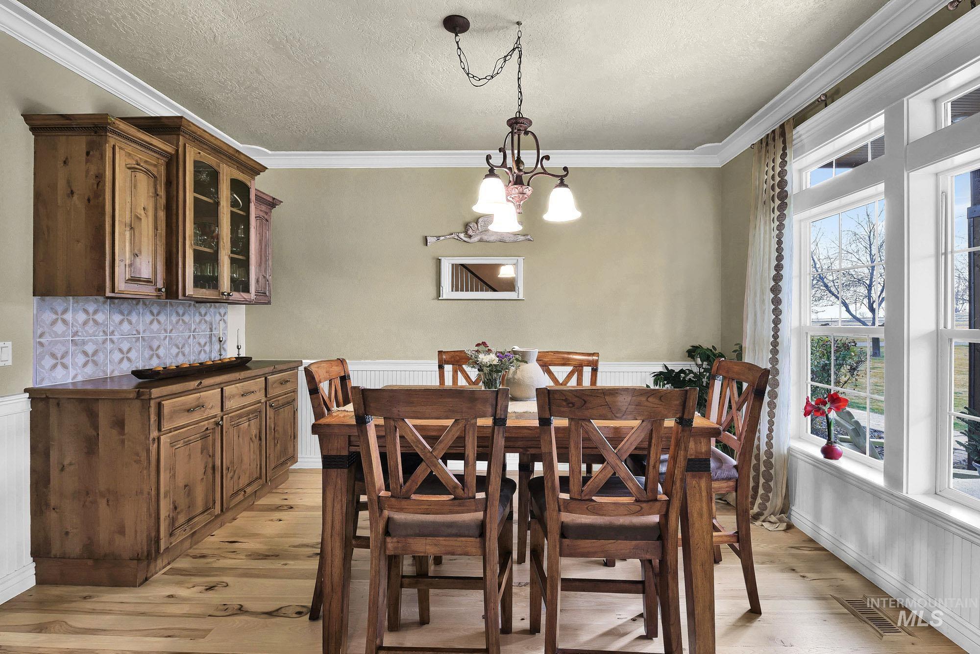 Dining room featuring light wood-style floors, hanging lights, crown molding, a textured ceiling, and wainscoting