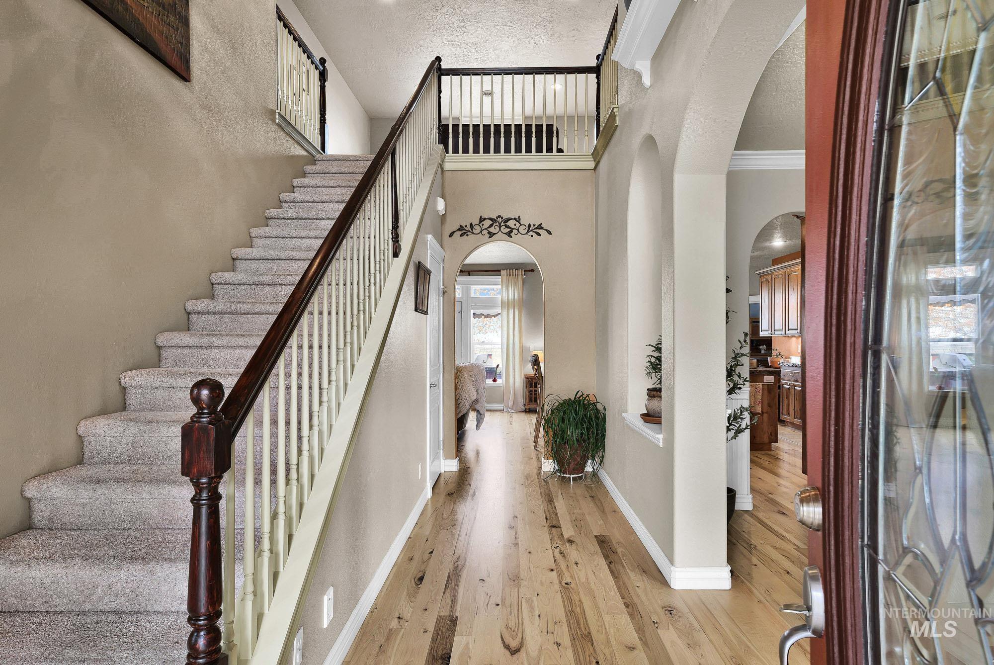 Foyer entrance featuring arched walkways, light wood-type flooring, a high textured ceiling, and ornamental molding