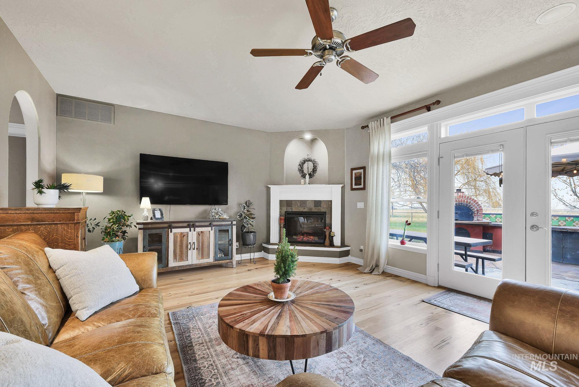 Living room featuring light wood-type flooring, ceiling fan, a tile fireplace, french doors, and arched walkways