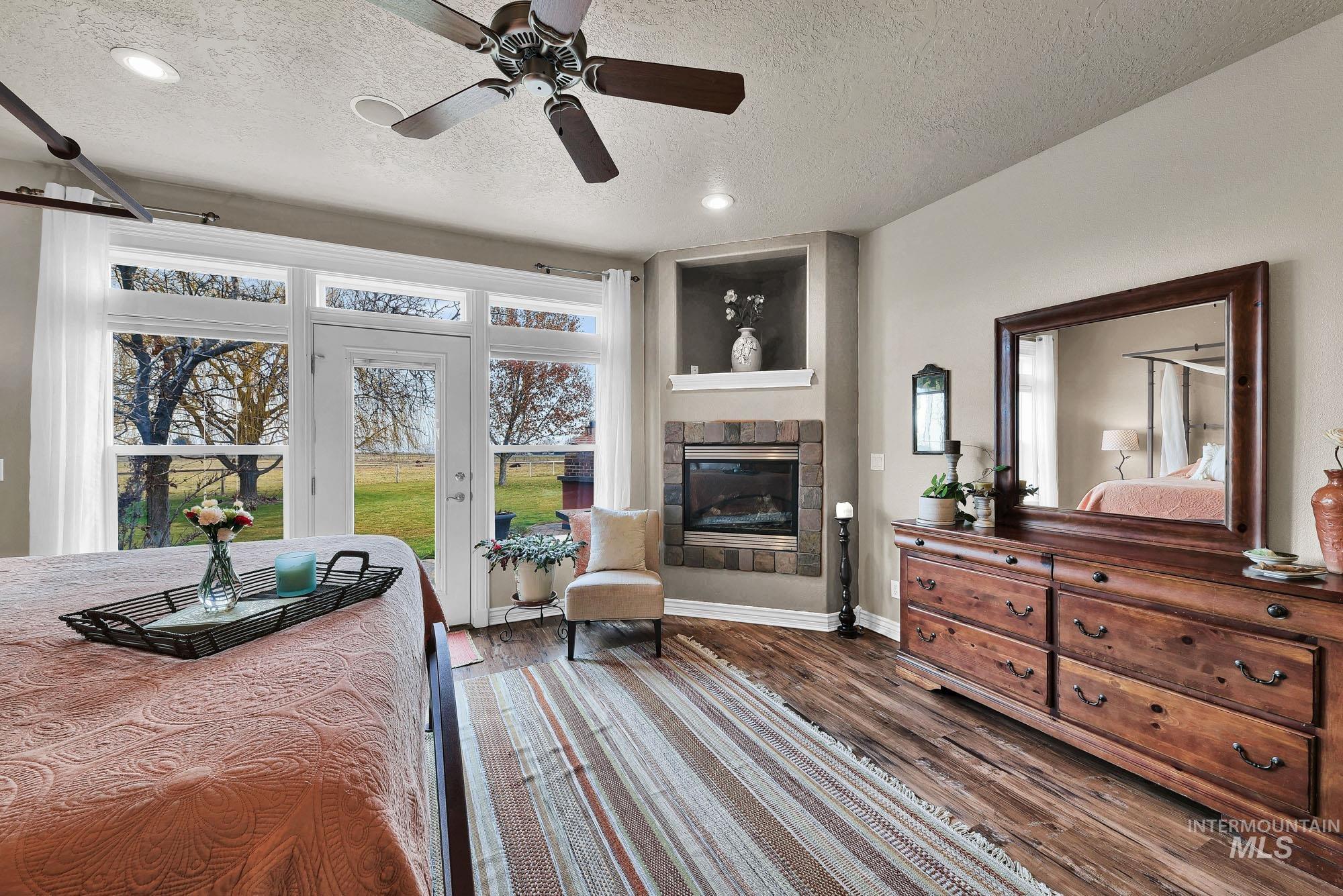 Bedroom with dark wood finished floors, a textured ceiling, a ceiling fan, a tile fireplace, and access to outside