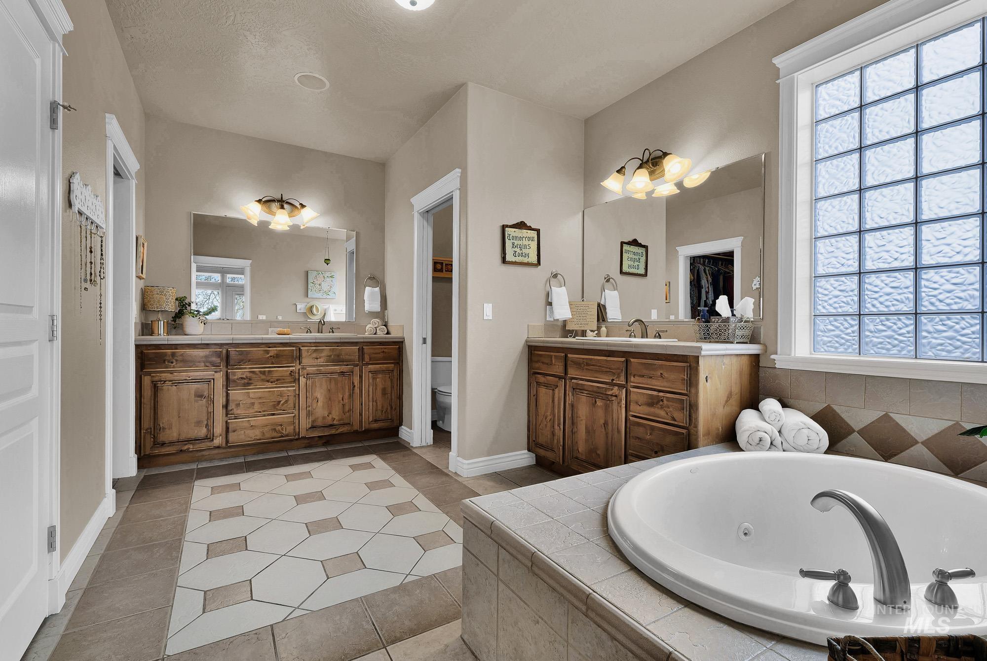 Primary bathroom featuring two vanities, light tile patterned floors, and a jacuzzi  tub