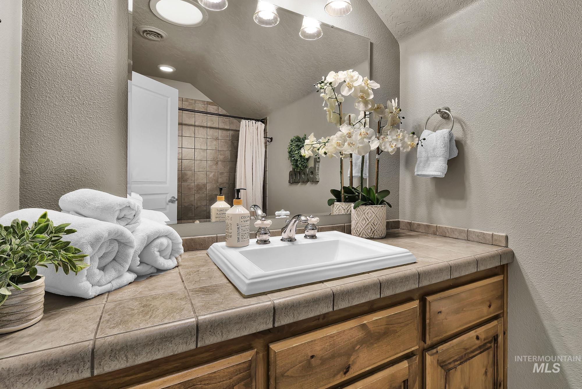 Full bath with a textured wall, skylight, vanity, tiled shower, and recessed lighting