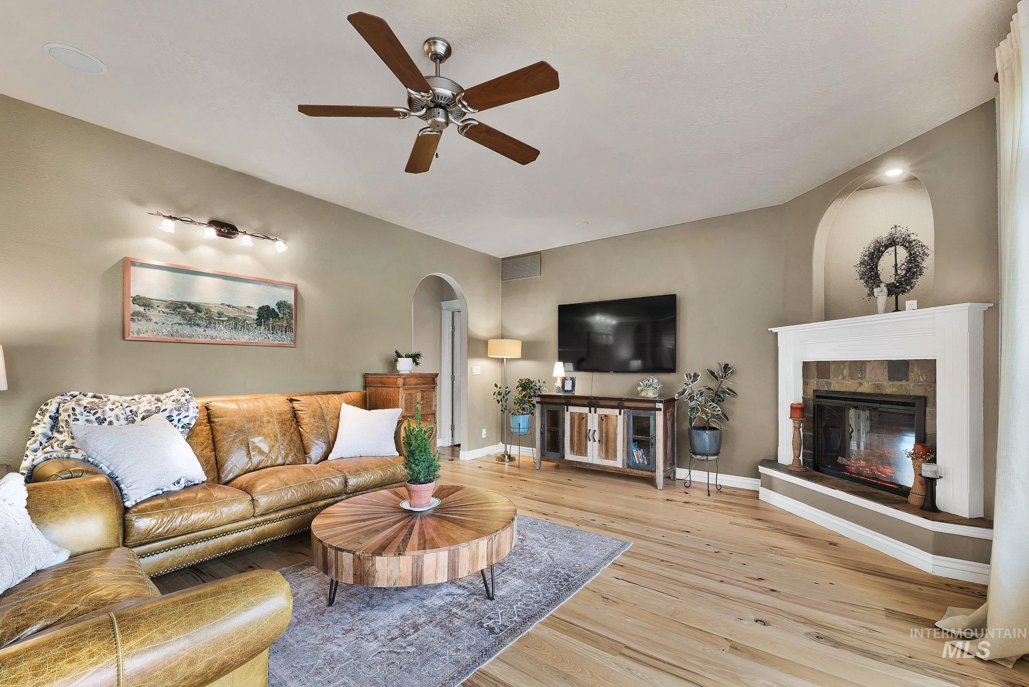 Living room with arched walkways, a ceiling fan, wood-type flooring, and a tiled fireplace