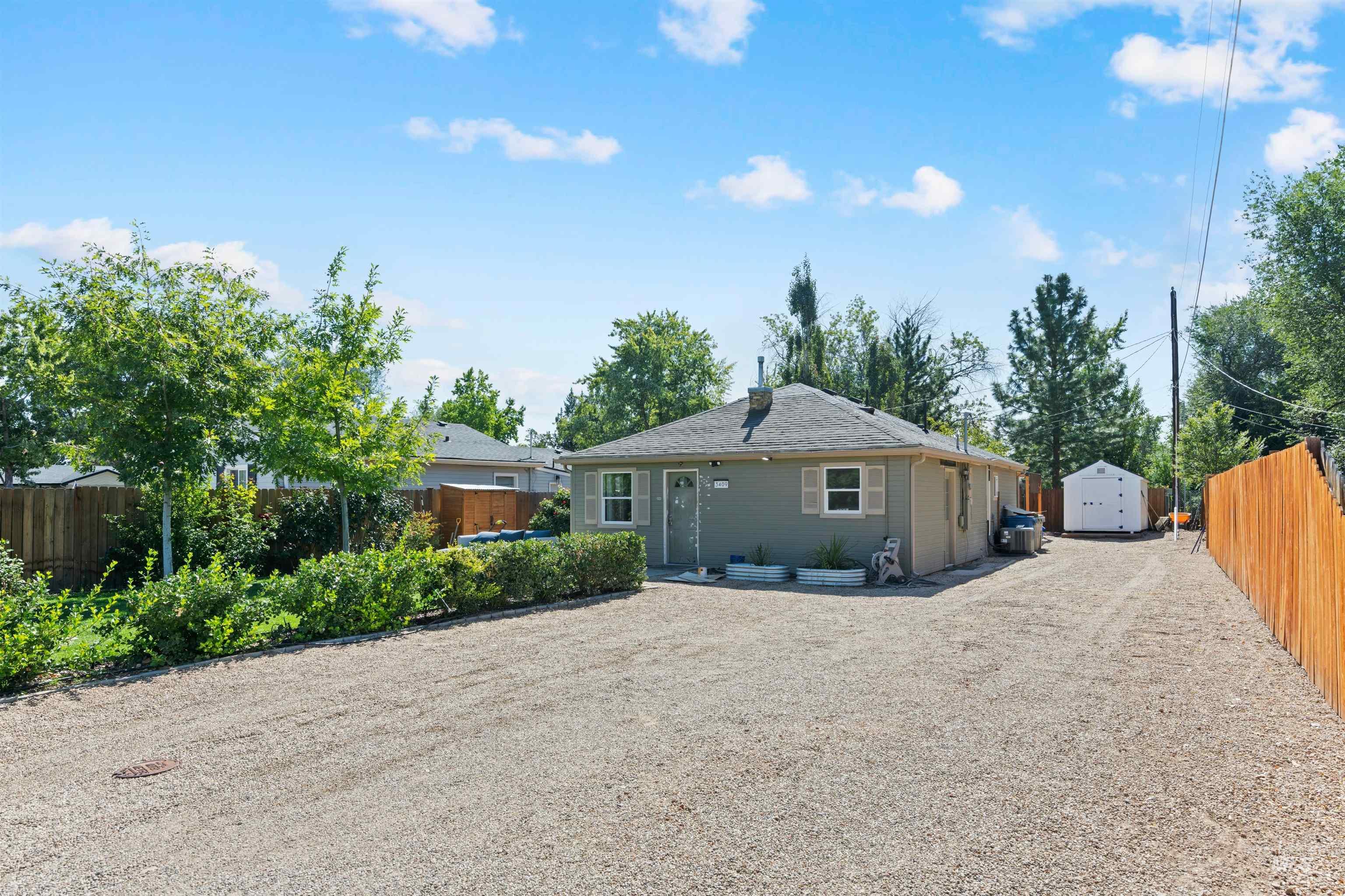 Back of property with a storage shed, a fenced backyard, gravel driveway, and a patio