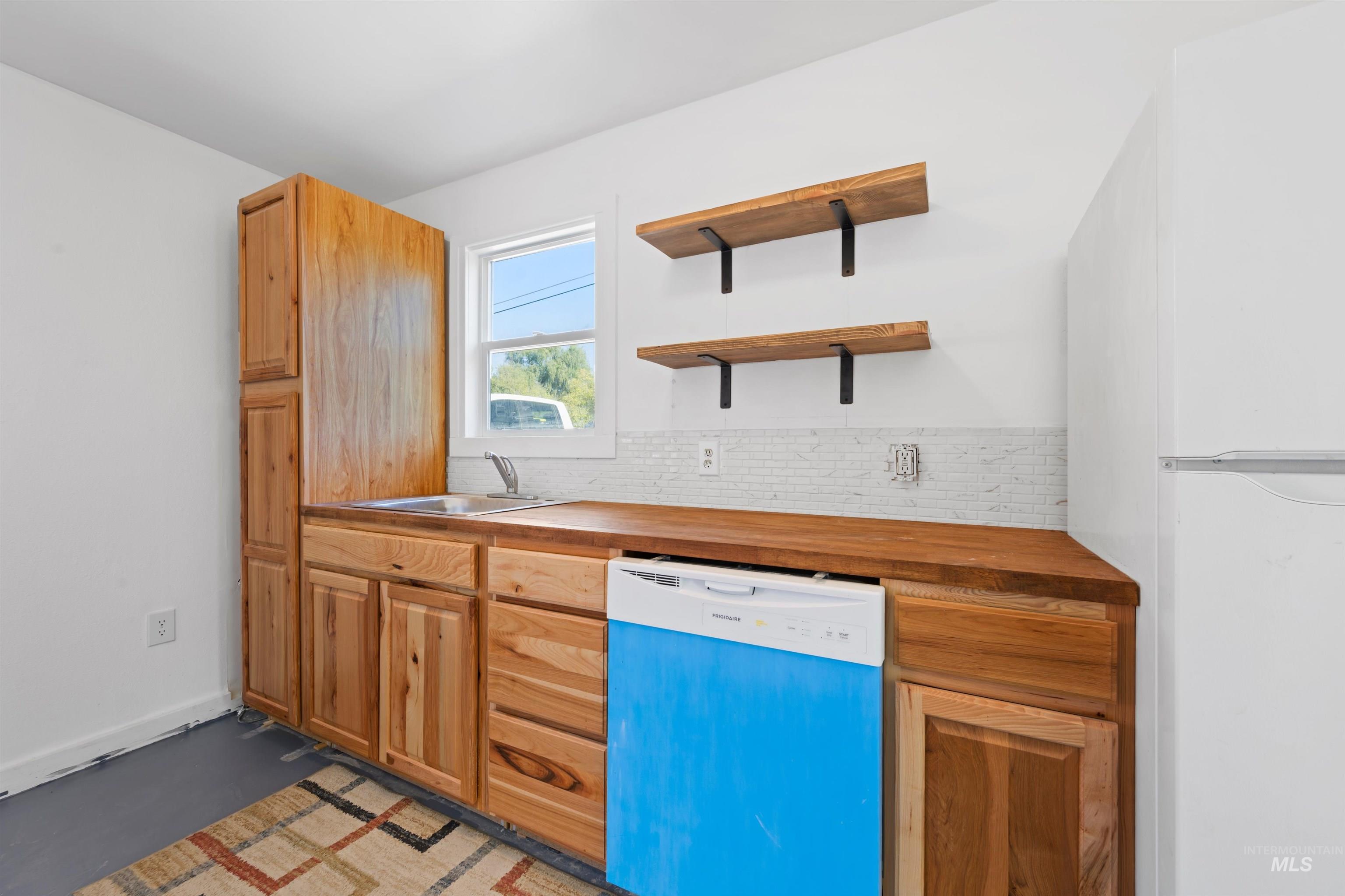 Kitchen with freestanding refrigerator, dishwashing machine, backsplash, open shelves, and butcher block countertops