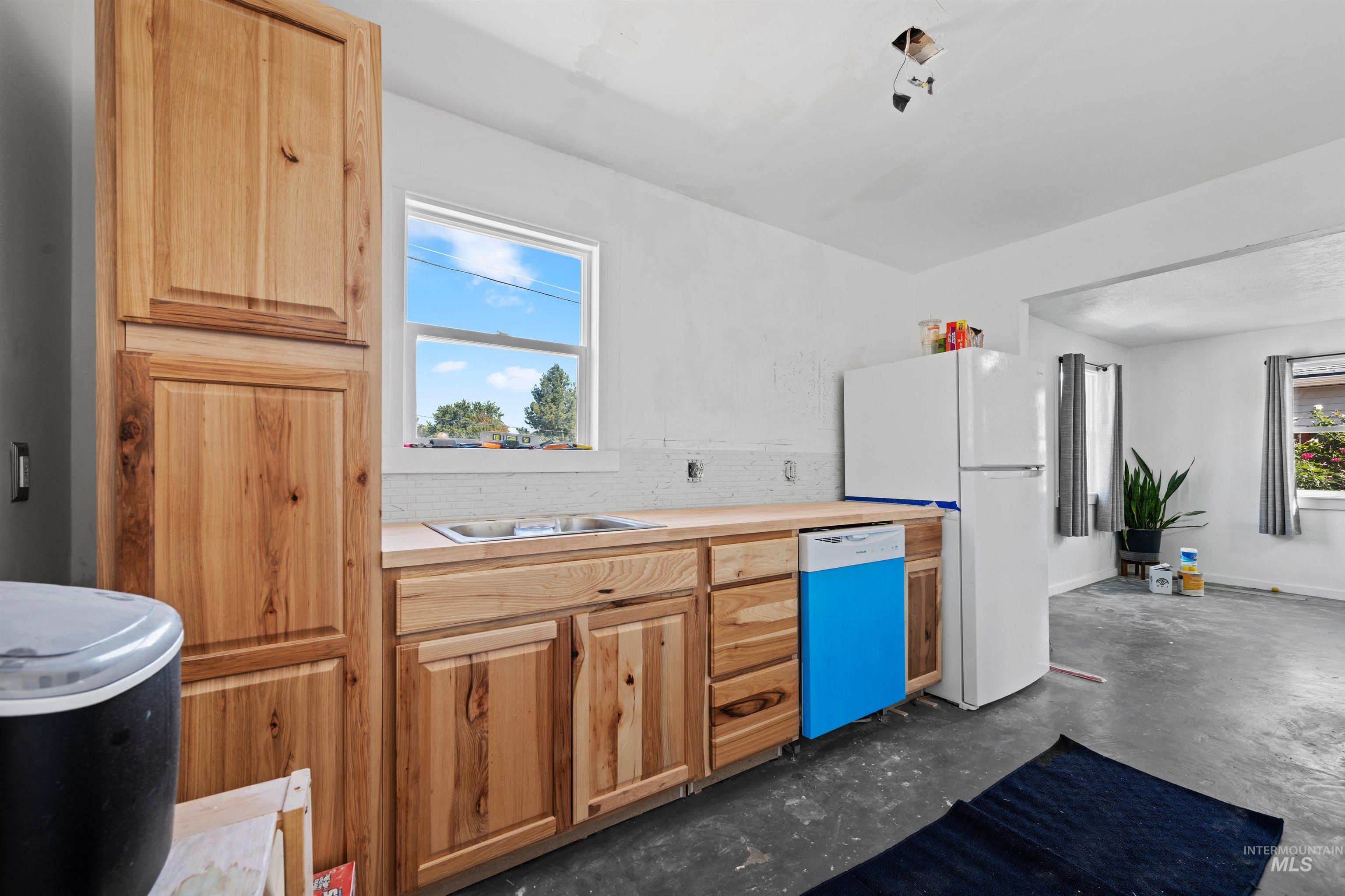 Kitchen with light countertops, concrete flooring, dishwashing machine, tasteful backsplash, and freestanding refrigerator