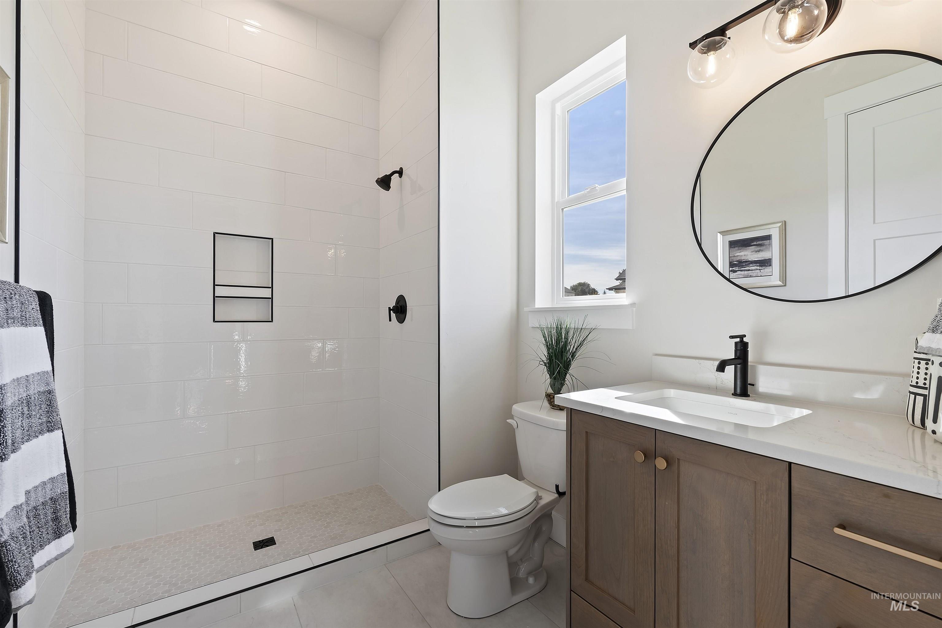 Full bath with vanity, tiled shower, and light tile patterned floors