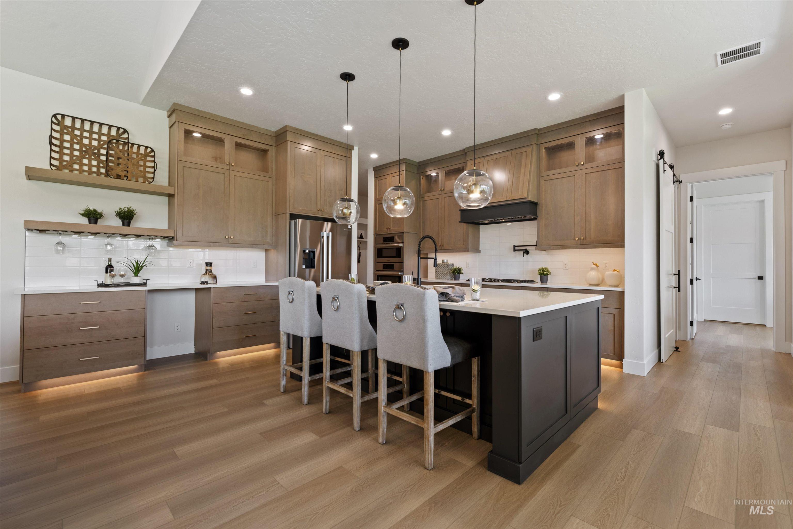 Kitchen featuring glass insert cabinets, stainless steel appliances, a center island with sink, a breakfast bar, and decorative light fixtures