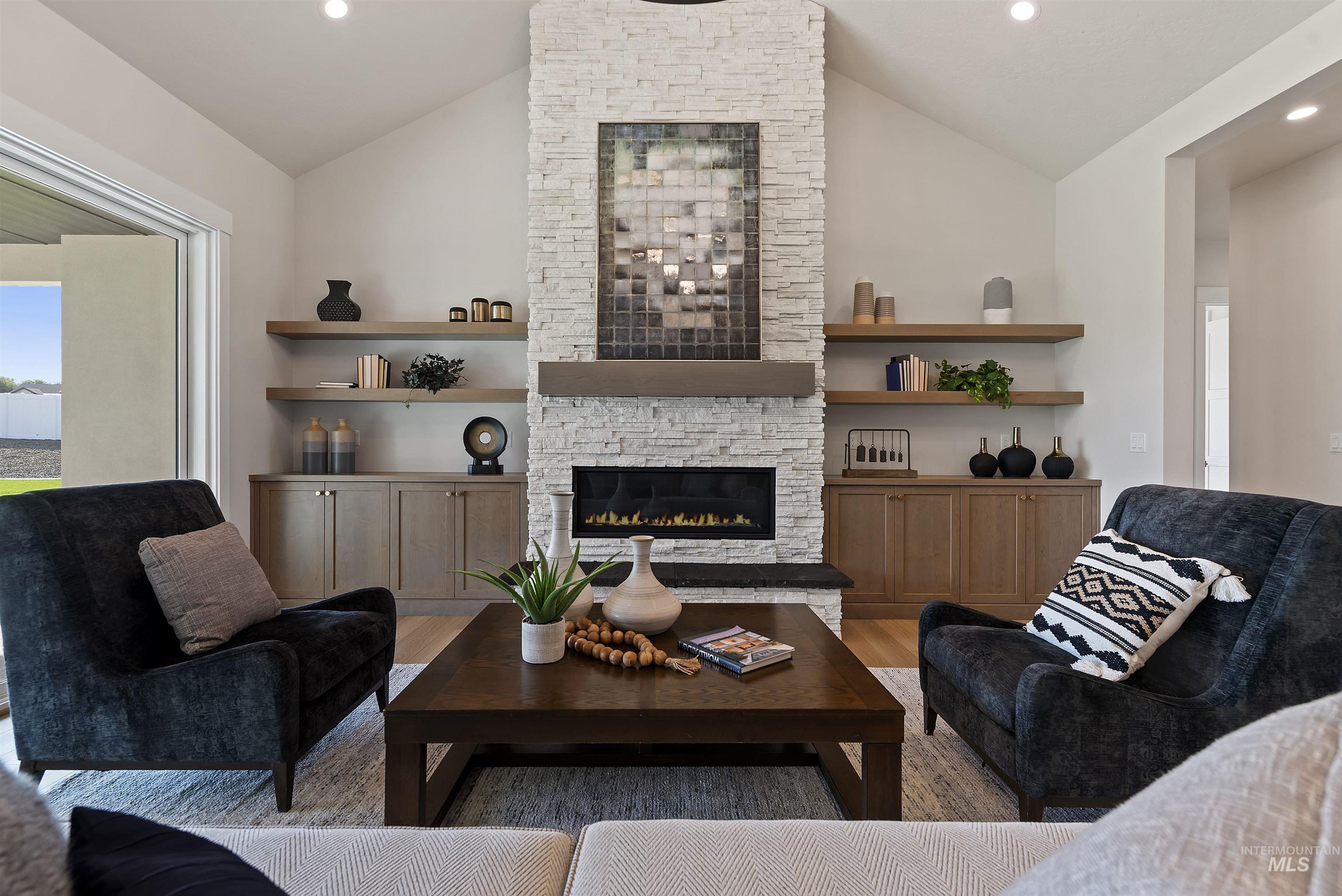 Living room featuring healthy amount of natural light, light wood-style flooring, lofted ceiling, recessed lighting, and a stone fireplace