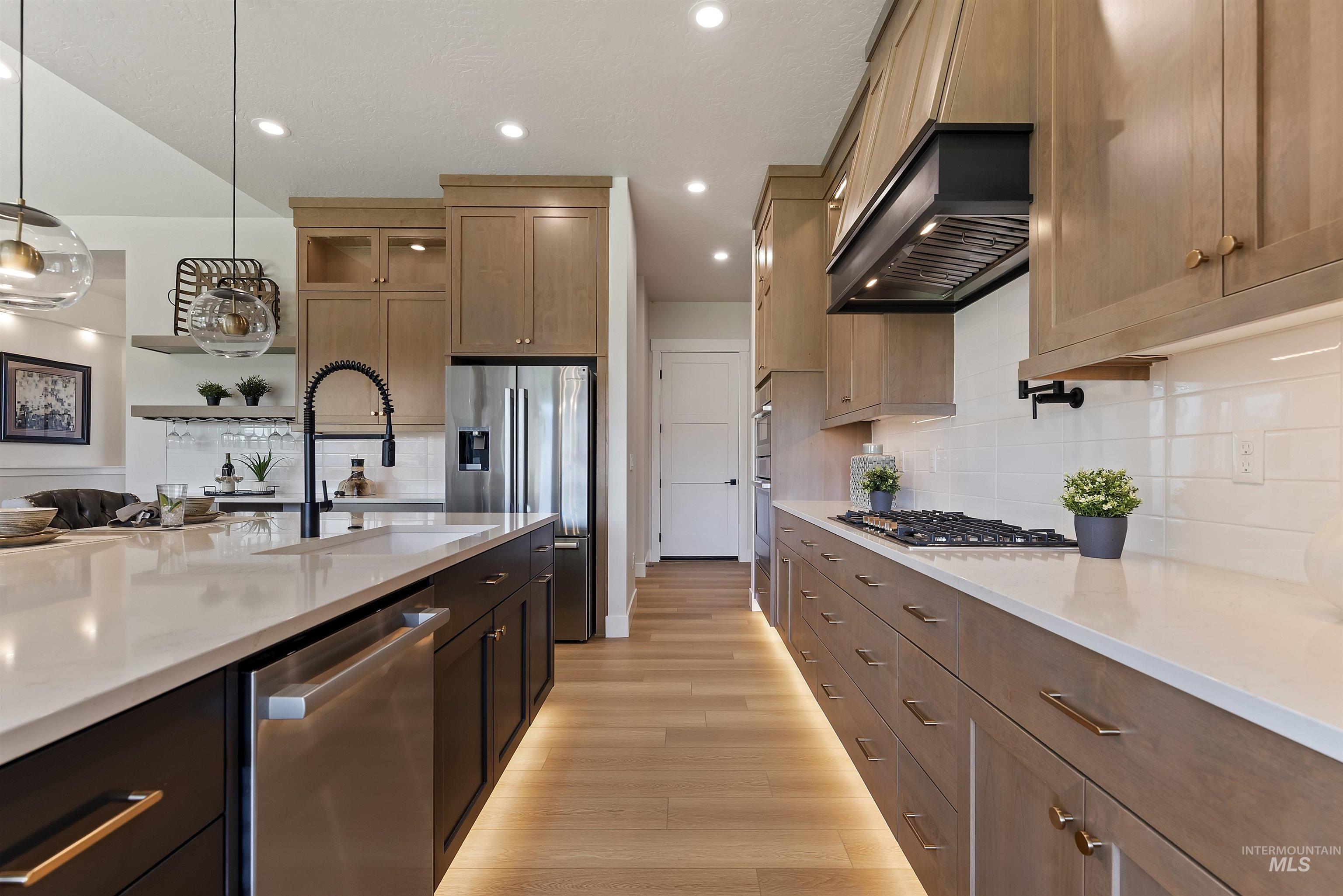 Kitchen with light stone countertops, stainless steel appliances, pendant lighting, light wood-style floors, and backsplash