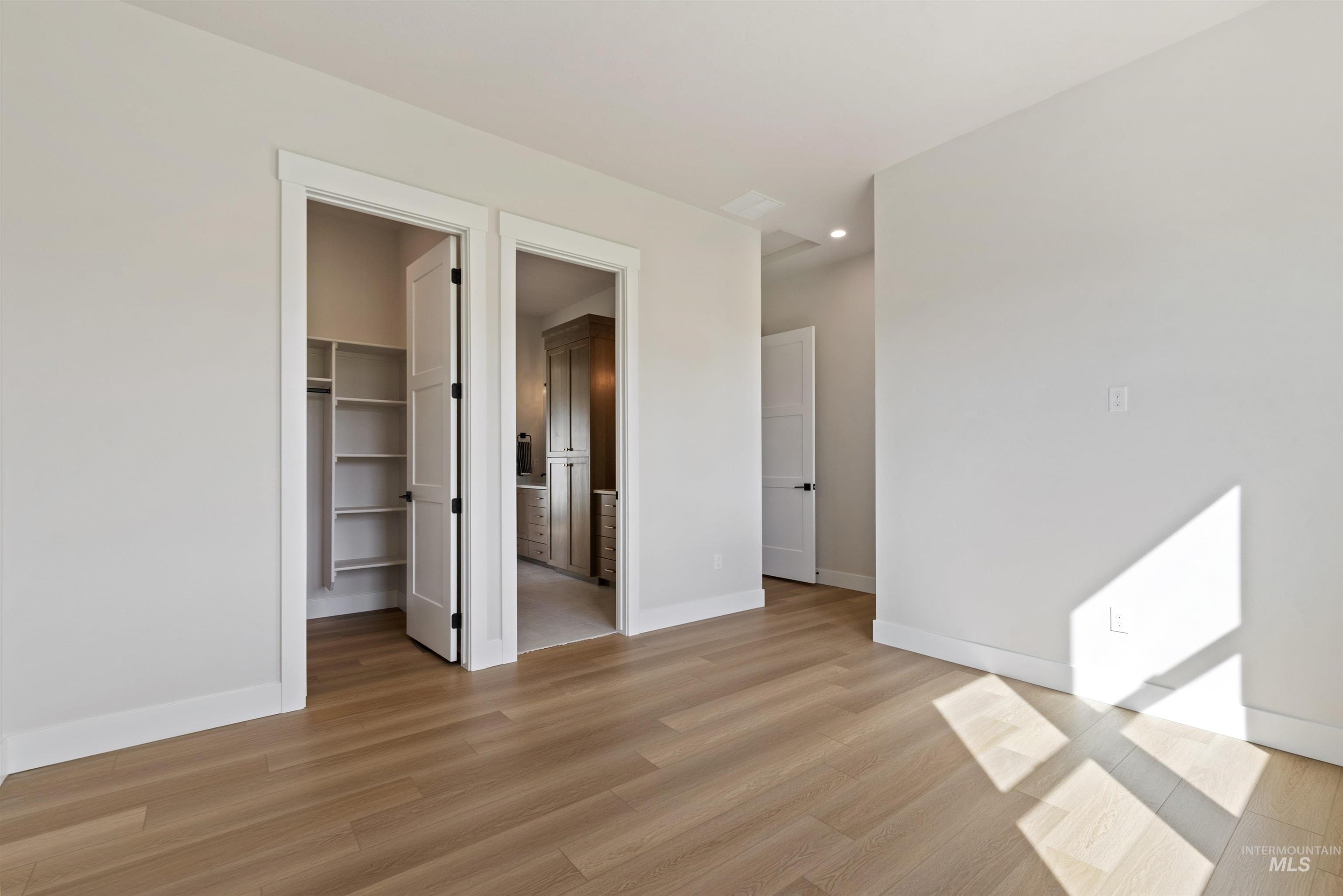 Unfurnished bedroom featuring connected bathroom, a spacious closet, and light wood-type flooring