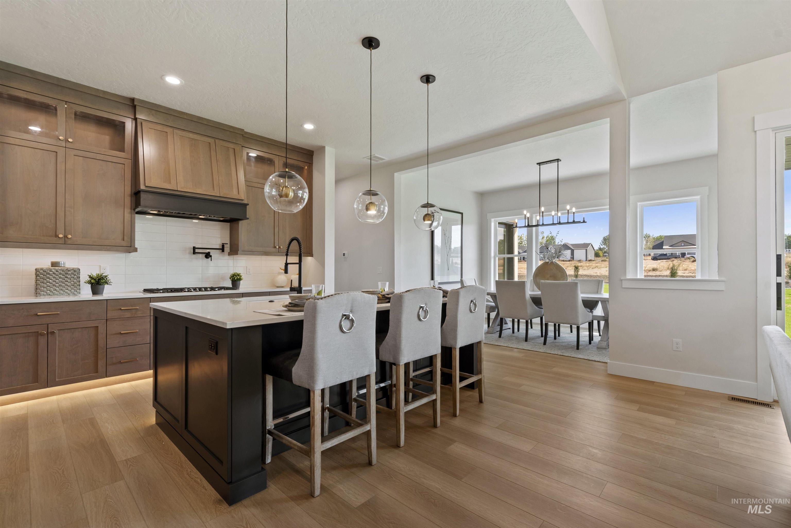 Kitchen featuring backsplash, decorative light fixtures, a breakfast bar area, a center island with sink, and light stone counters