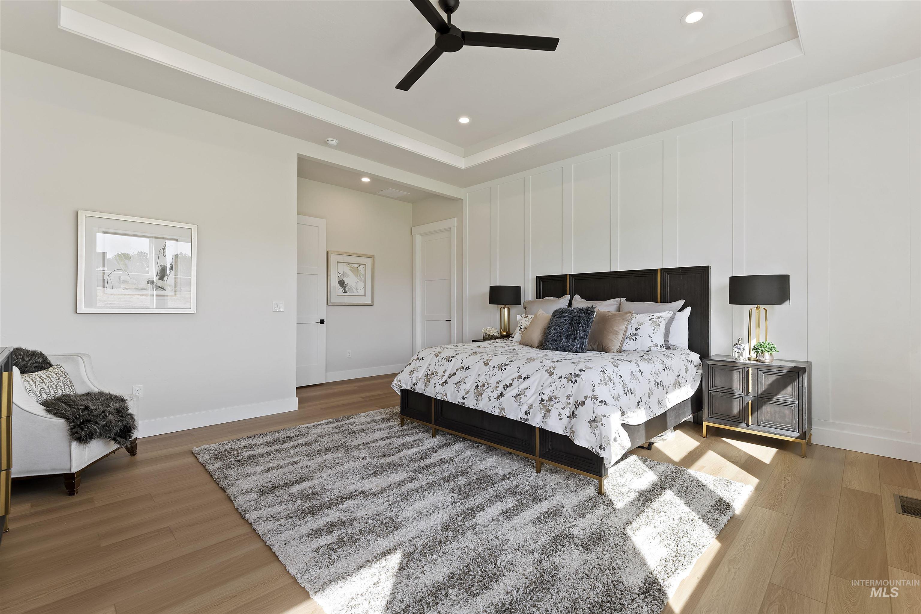 Bedroom featuring a tray ceiling, recessed lighting, light wood-style floors, ceiling fan, and a decorative wall
