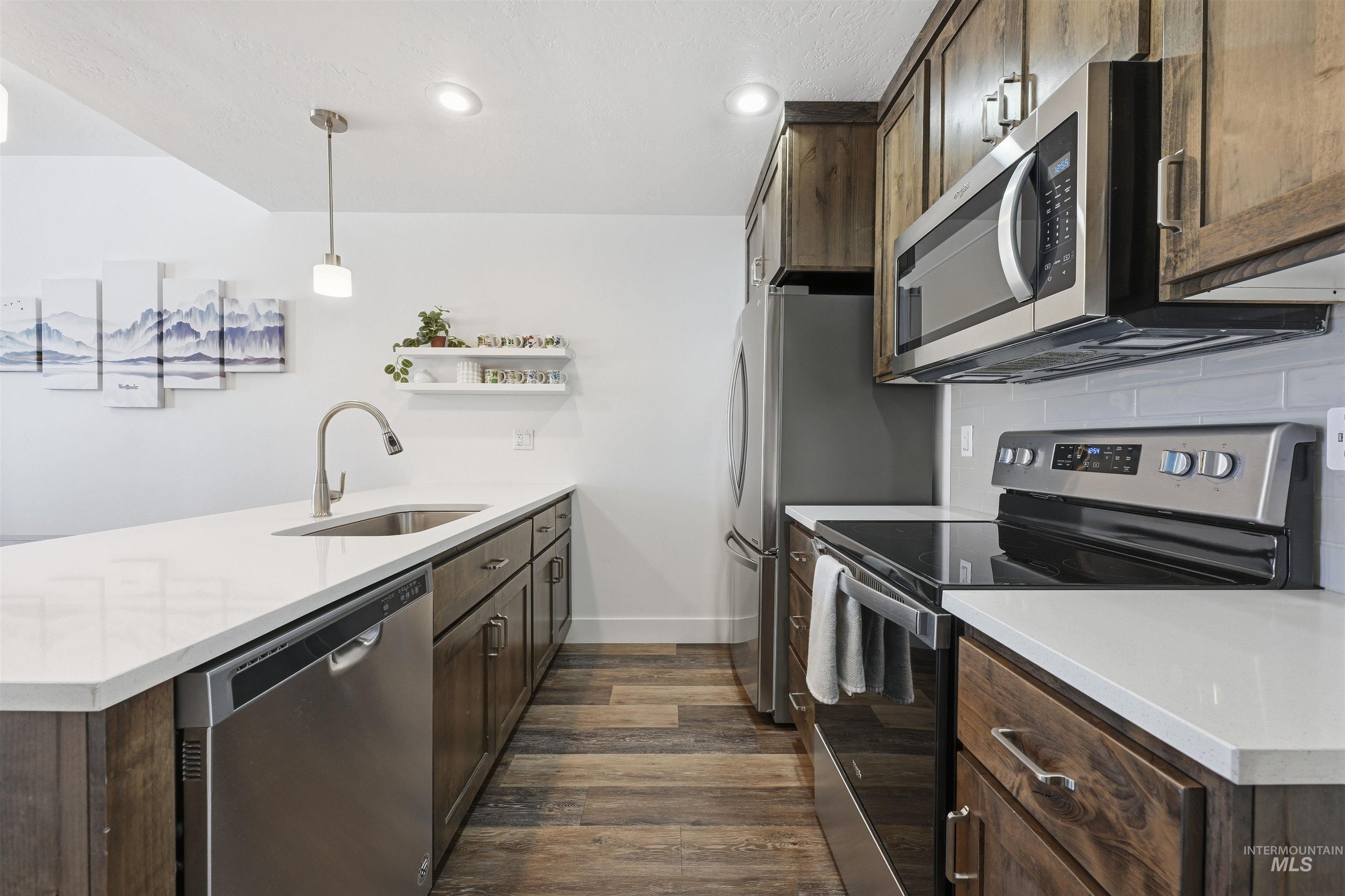 Two tone kitchen featuring stainless steel appliances, a peninsula, pendant lighting, open shelves, and light stone counters