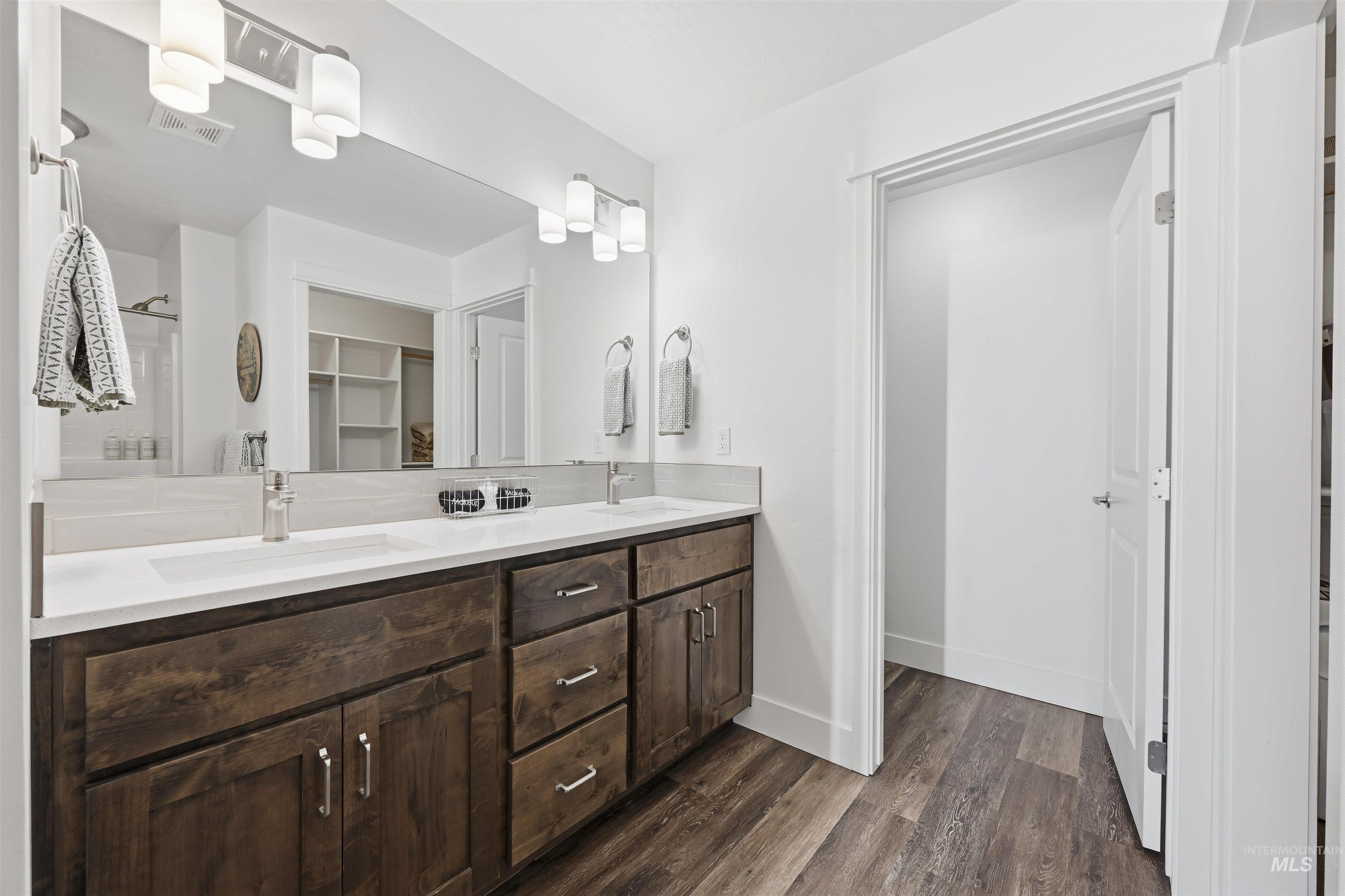 Bathroom featuring double vanity, dark wood-type flooring, a spacious closet, and a shower