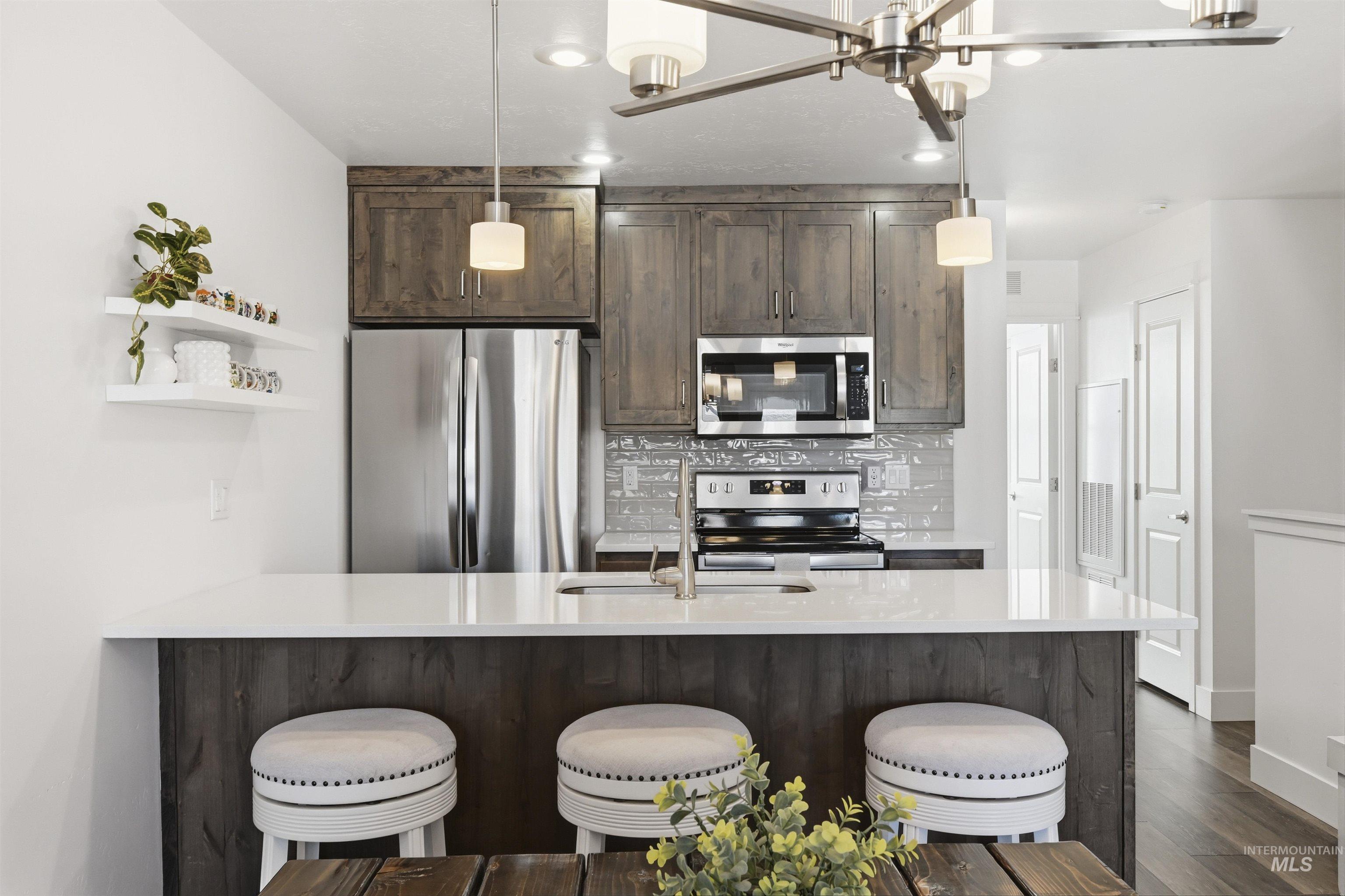 Kitchen with dark wood finish cabinetry, stainless steel appliances, light stone counters, open shelves, and a kitchen breakfast bar