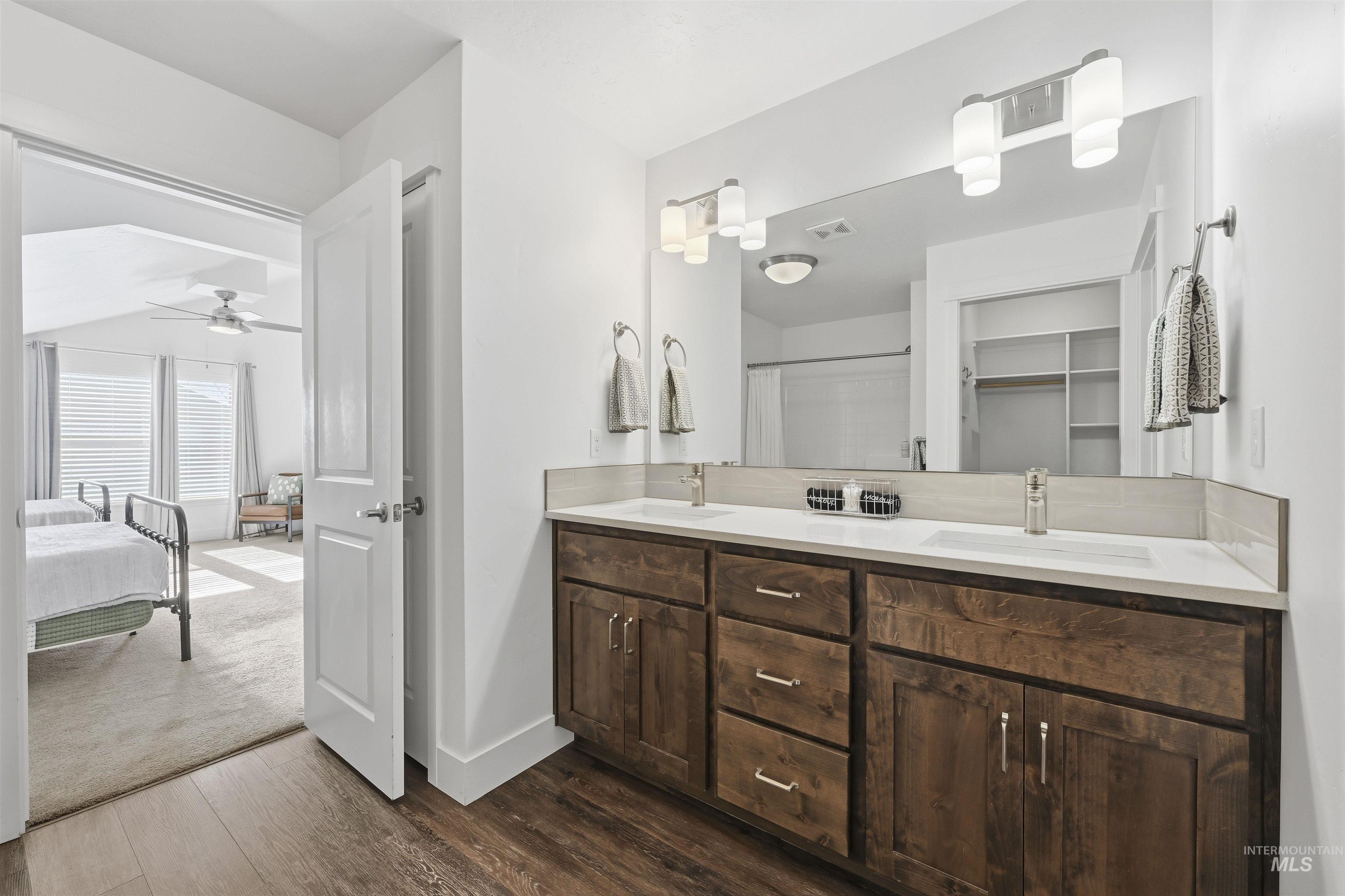 Full bath featuring double vanity, a shower with shower curtain, dark wood finished floors, and a spacious closet