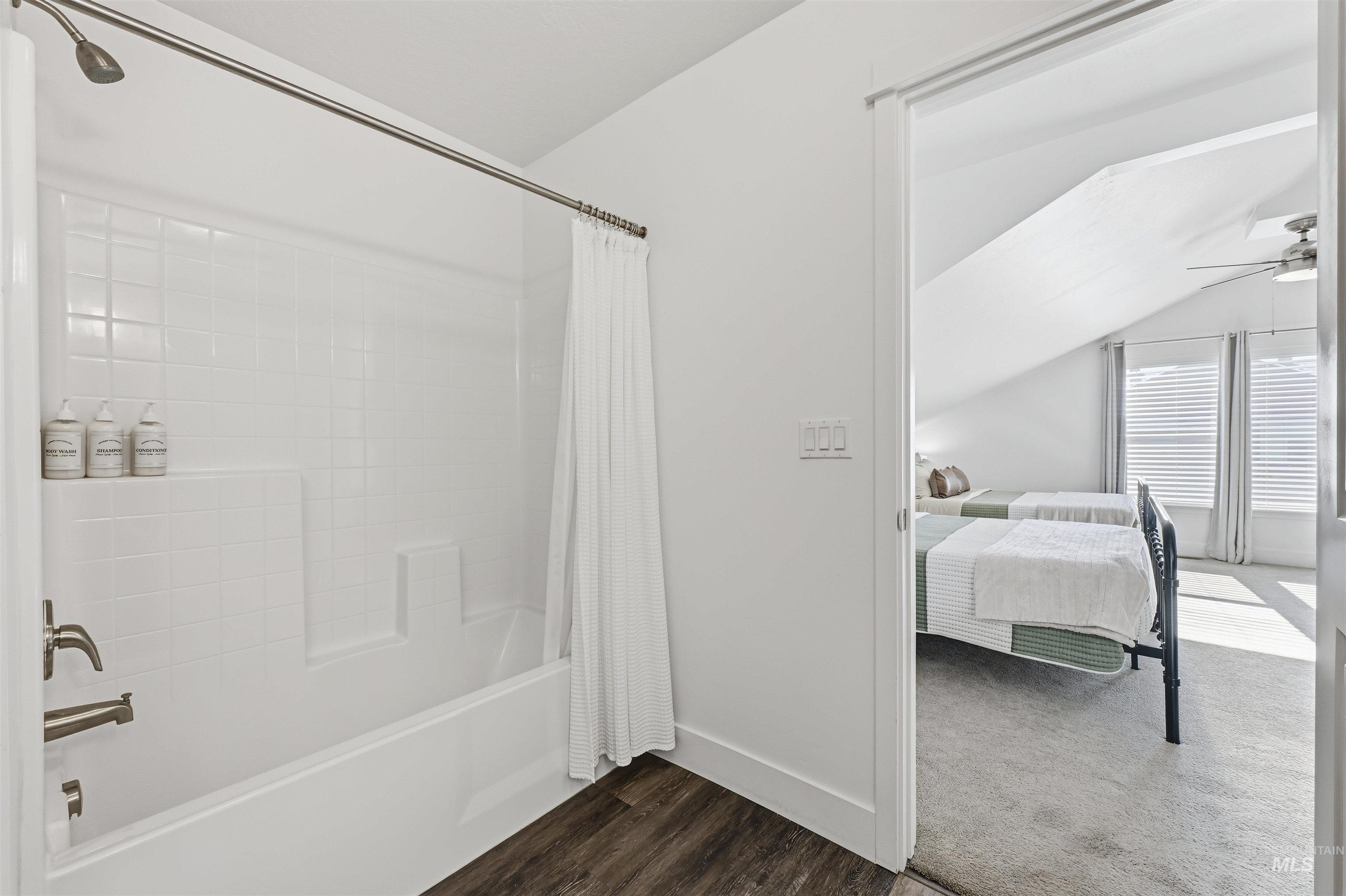 Ensuite bathroom featuring shower / tub combo, ceiling fan, dark wood finished floors, and lofted ceiling