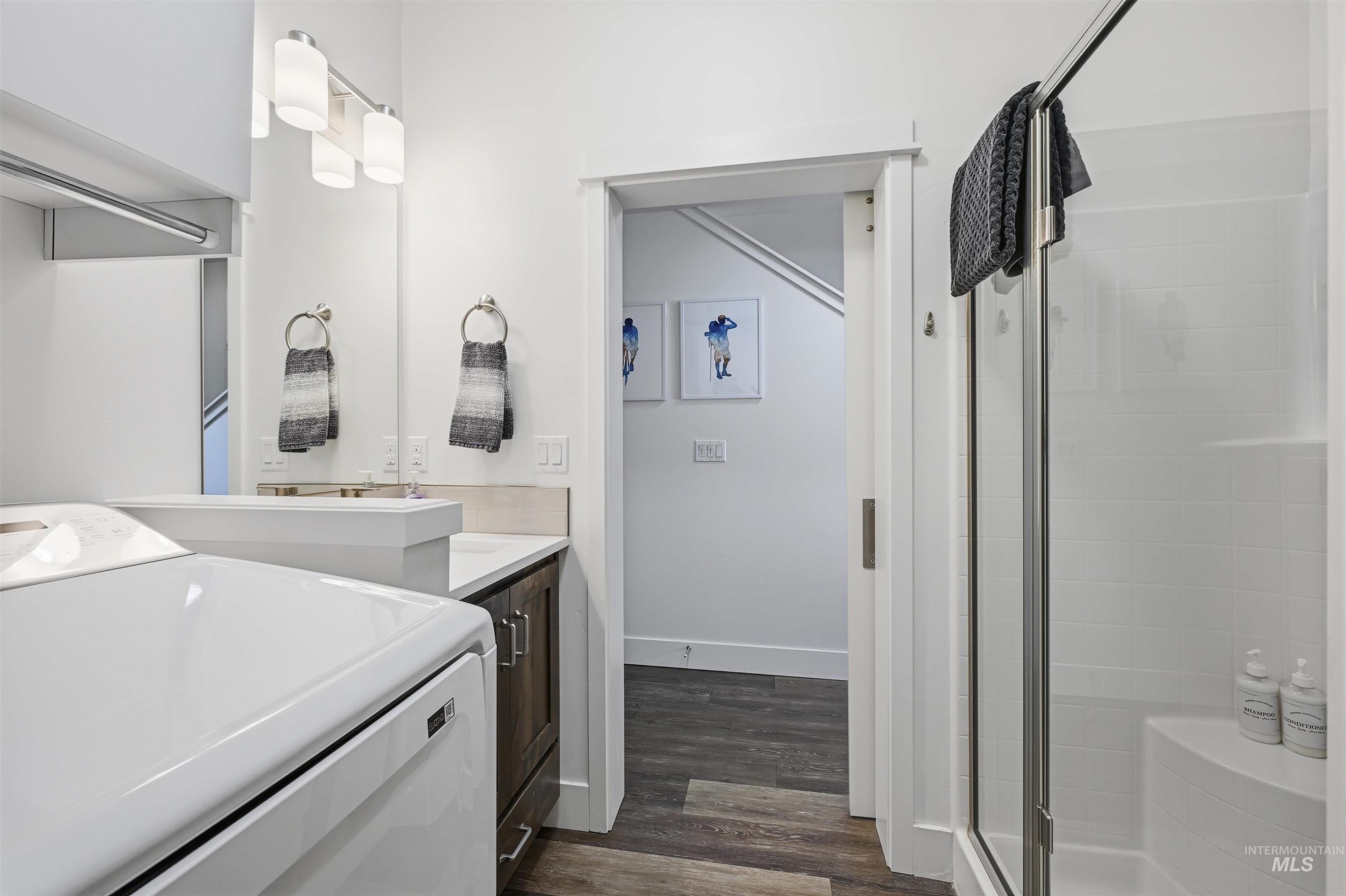 Full bath with washer / dryer, vanity, a stall shower, and dark wood-style flooring