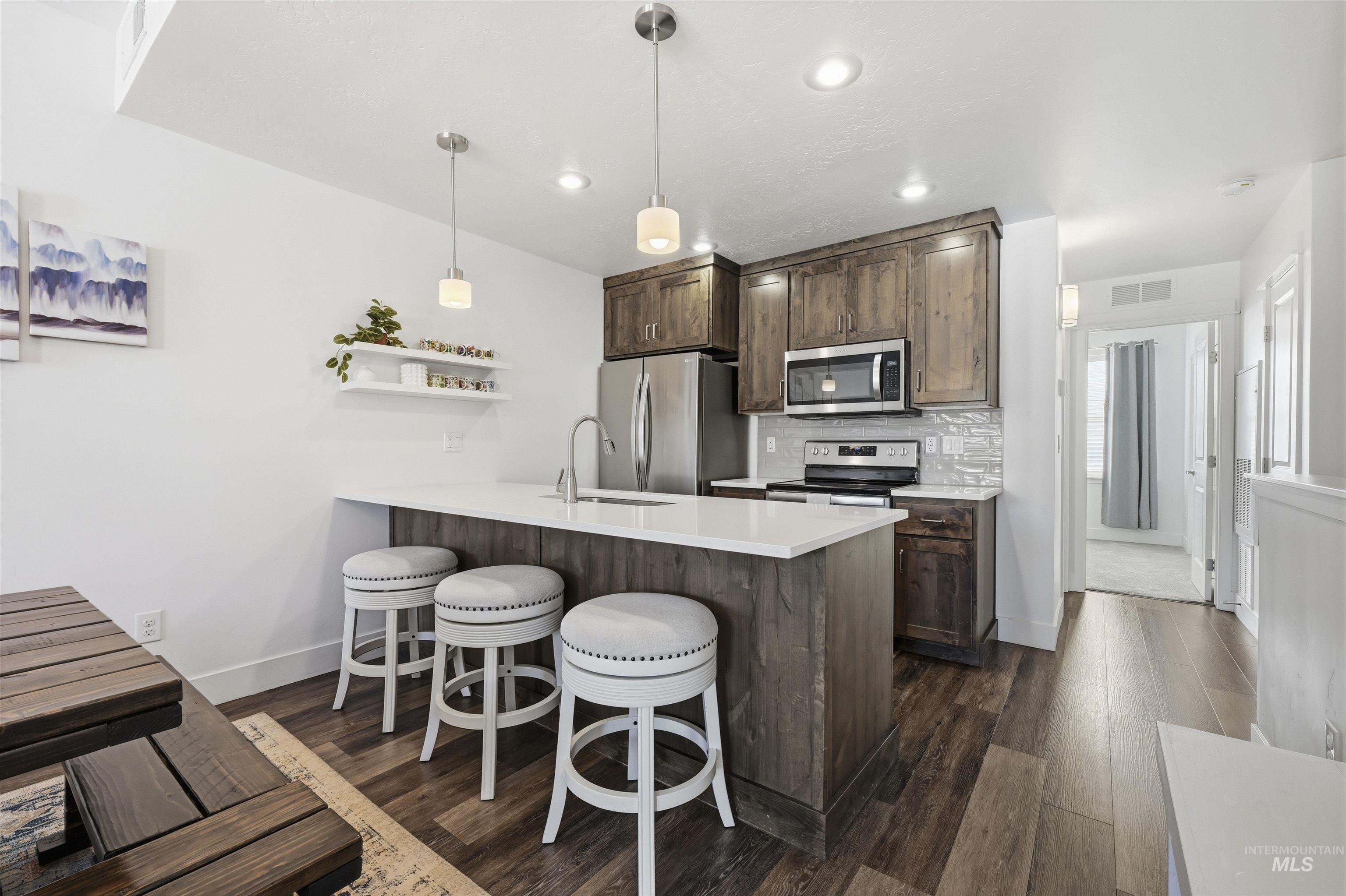 Kitchen with open shelves, dark wood-style floors, dark wood finish cabinetry, a peninsula, and stainless steel appliances