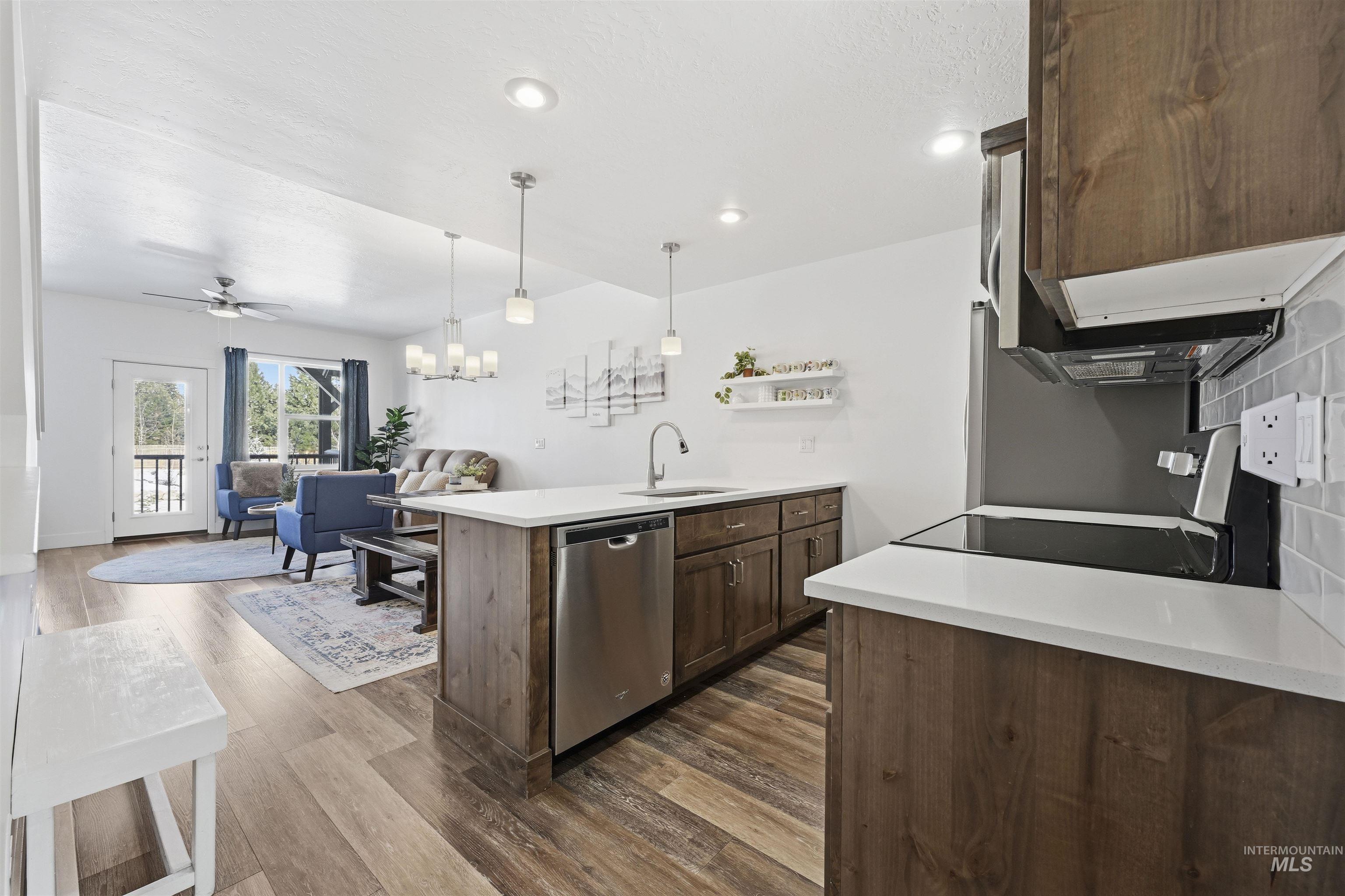 Kitchen featuring a peninsula, hanging lights, dark wood finish cabinets, dishwasher, and open floor plan