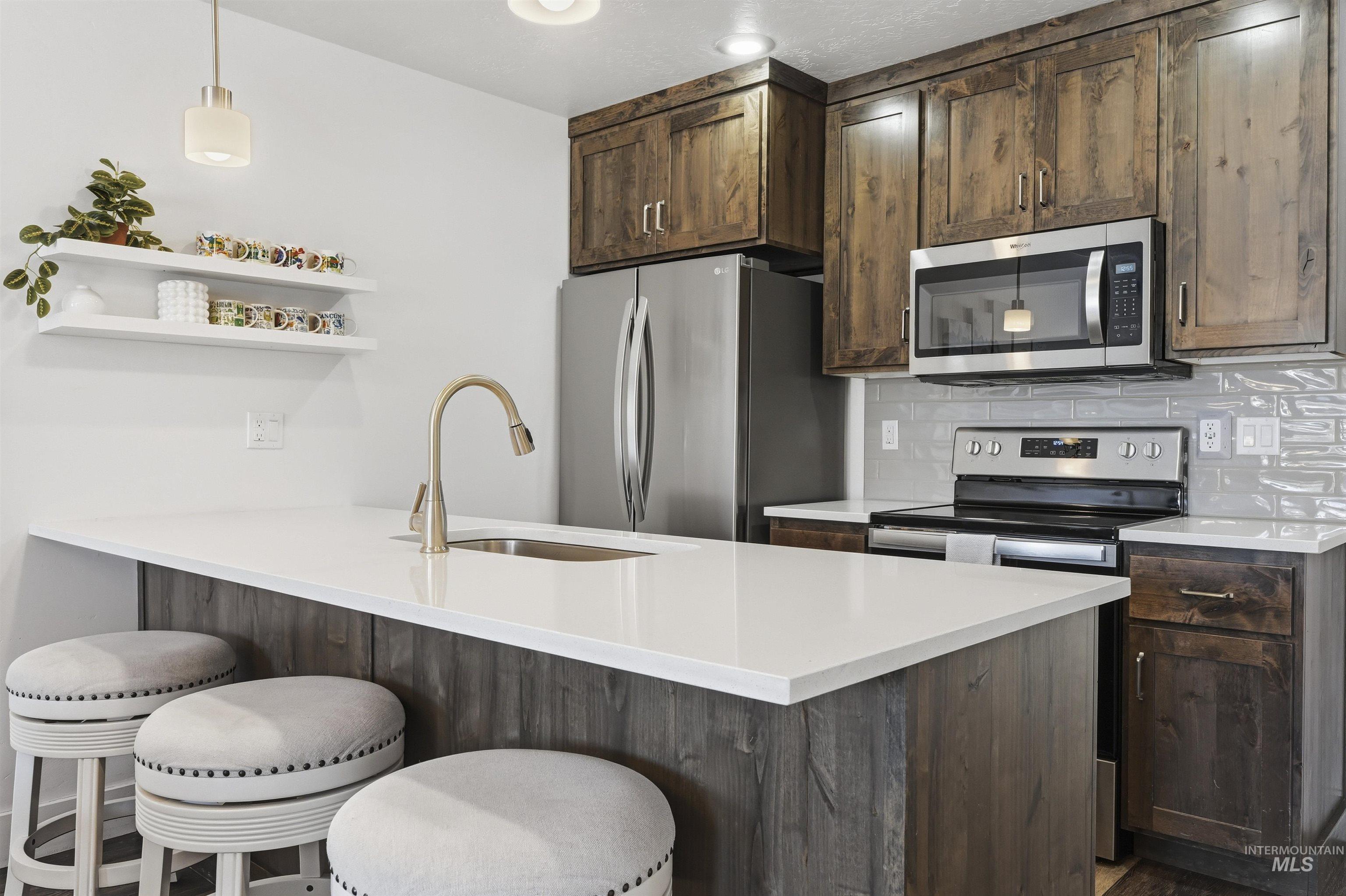 Kitchen featuring pendant lighting, a peninsula, stainless steel appliances, open shelves, and a kitchen bar