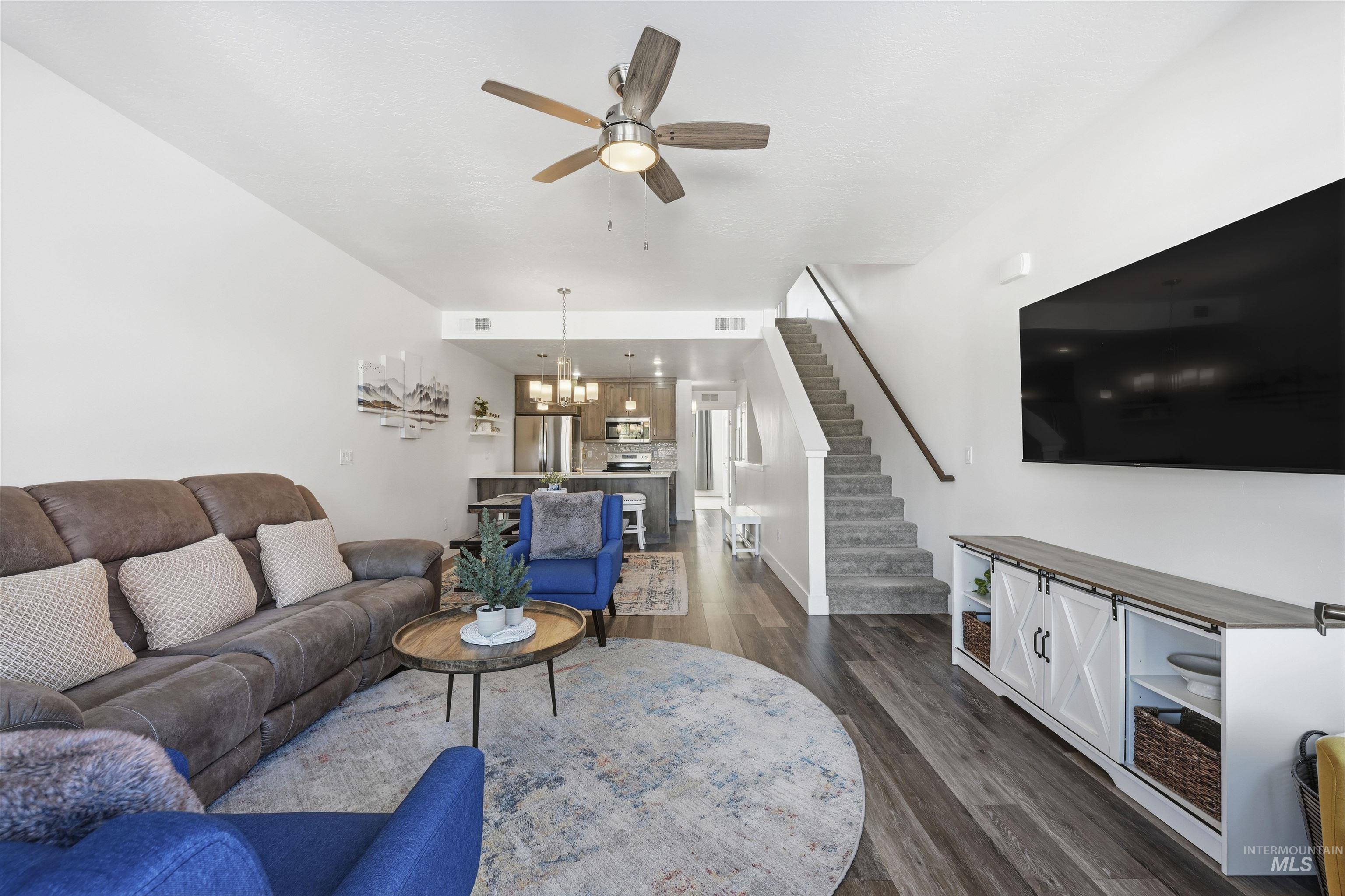 Living area with ceiling fan, hanging lights, and dark wood-style flooring