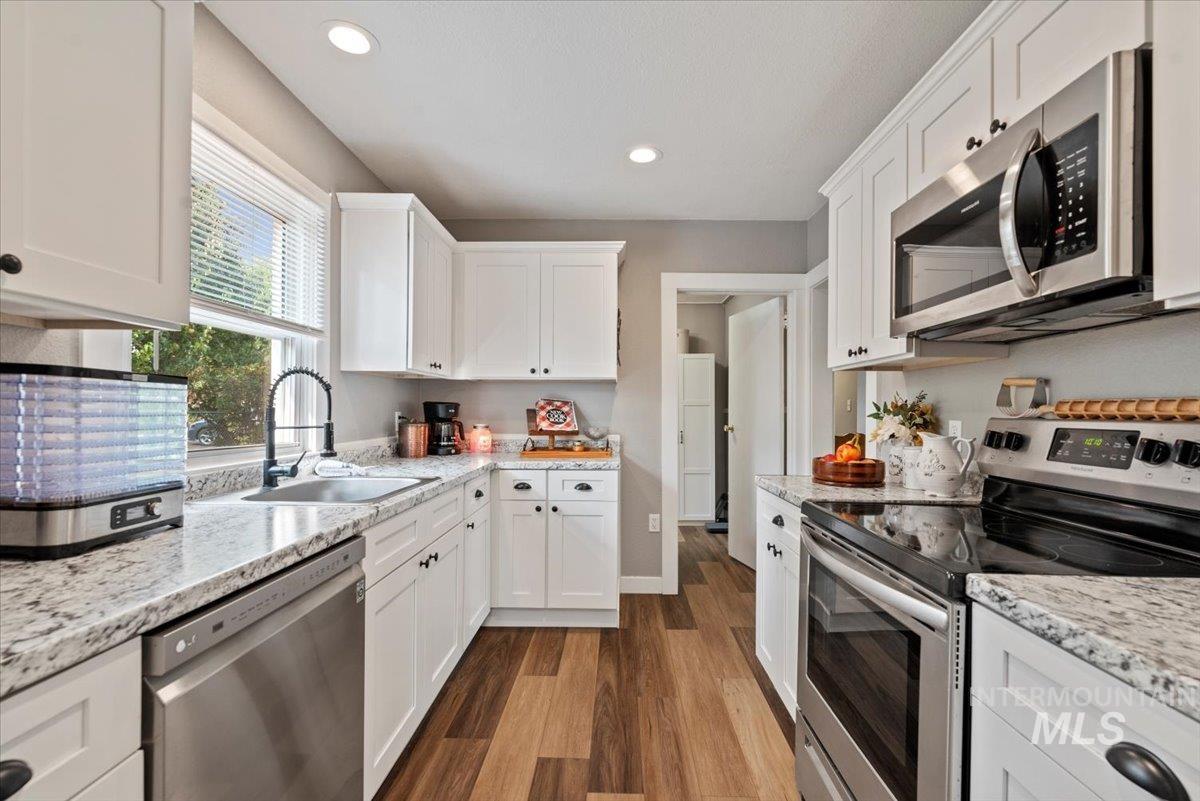 Kitchen with appliances with stainless steel finishes, dark wood-style flooring, white cabinets, light stone counters, and recessed lighting