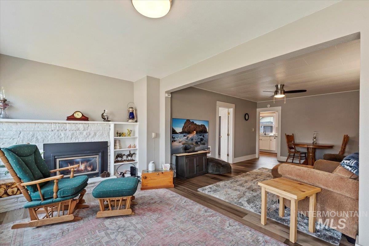 Living room featuring wood finished floors, a glass covered fireplace, and a ceiling fan
