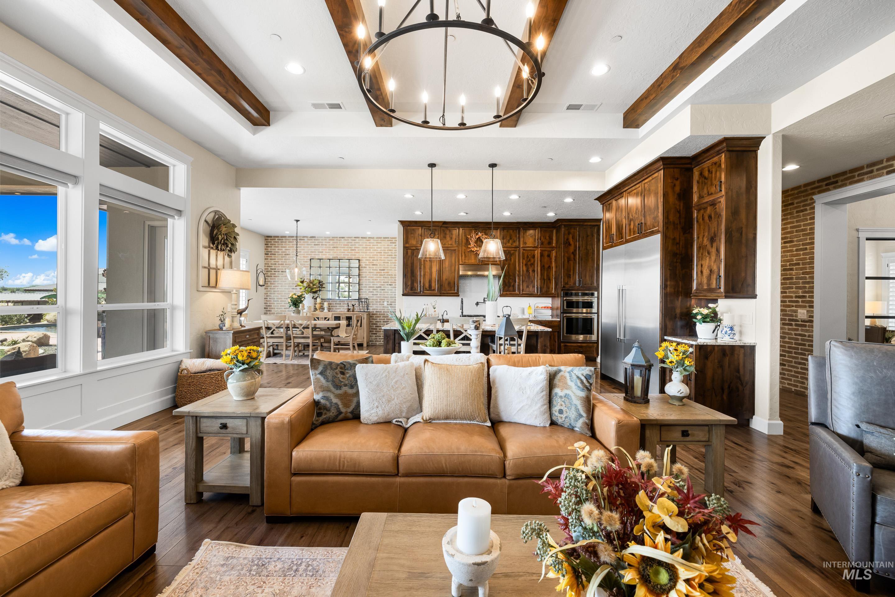 Living room with dark wood-style flooring, a chandelier, beam ceiling, brick wall, and recessed lighting