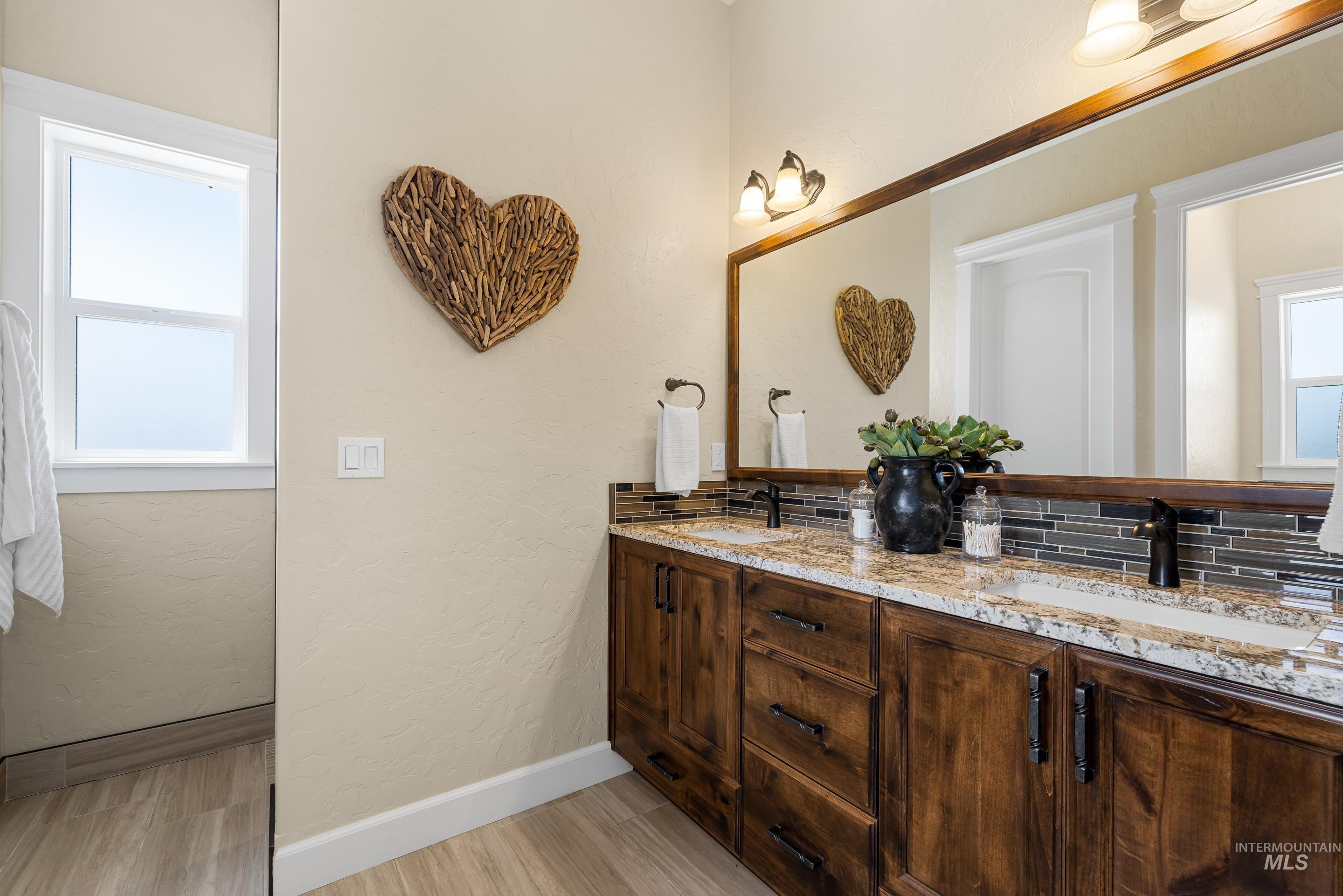 Bathroom featuring double vanity, wood finished floors, a textured wall, and backsplash
