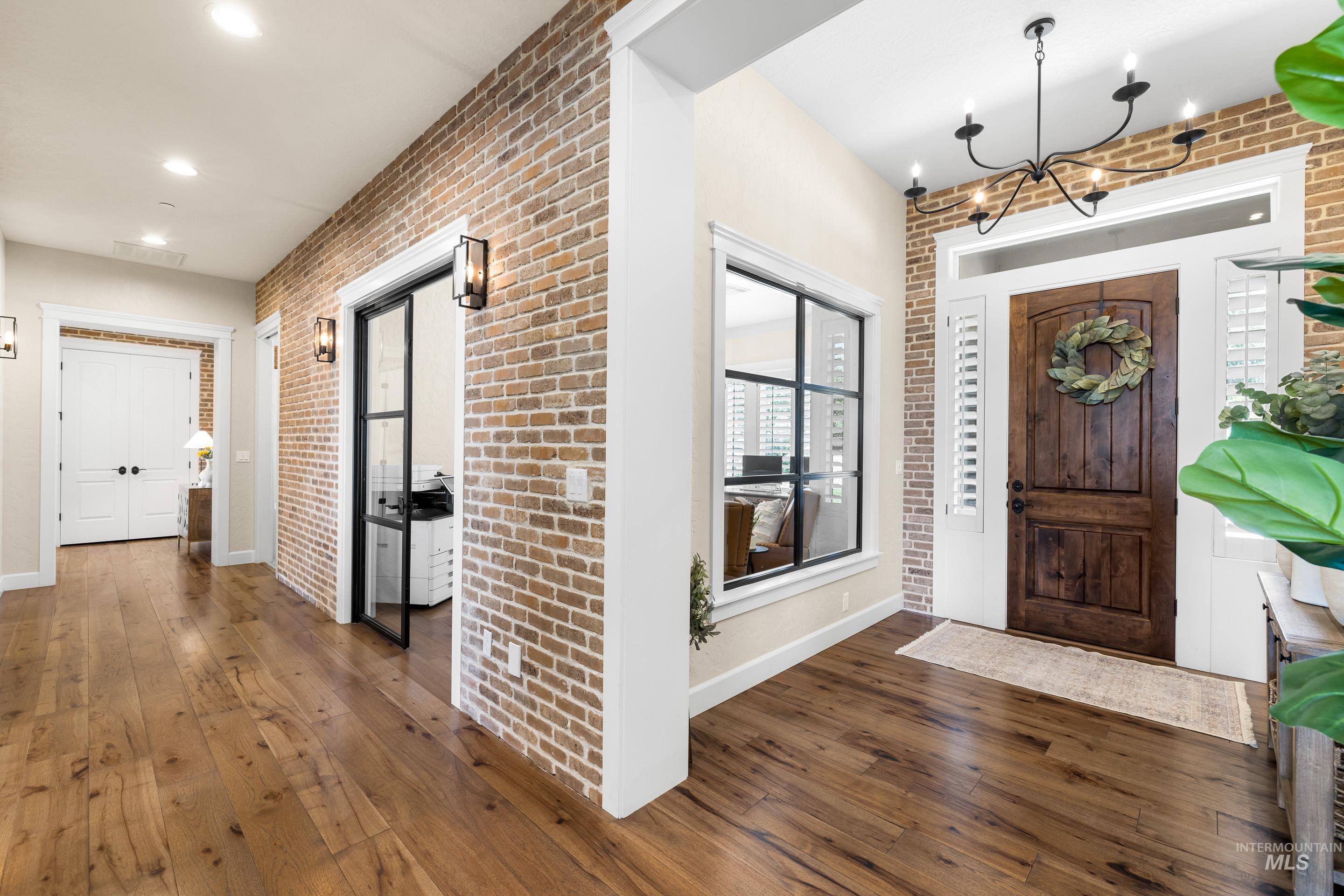 Foyer entrance featuring brick wall, wood-type flooring, and a chandelier