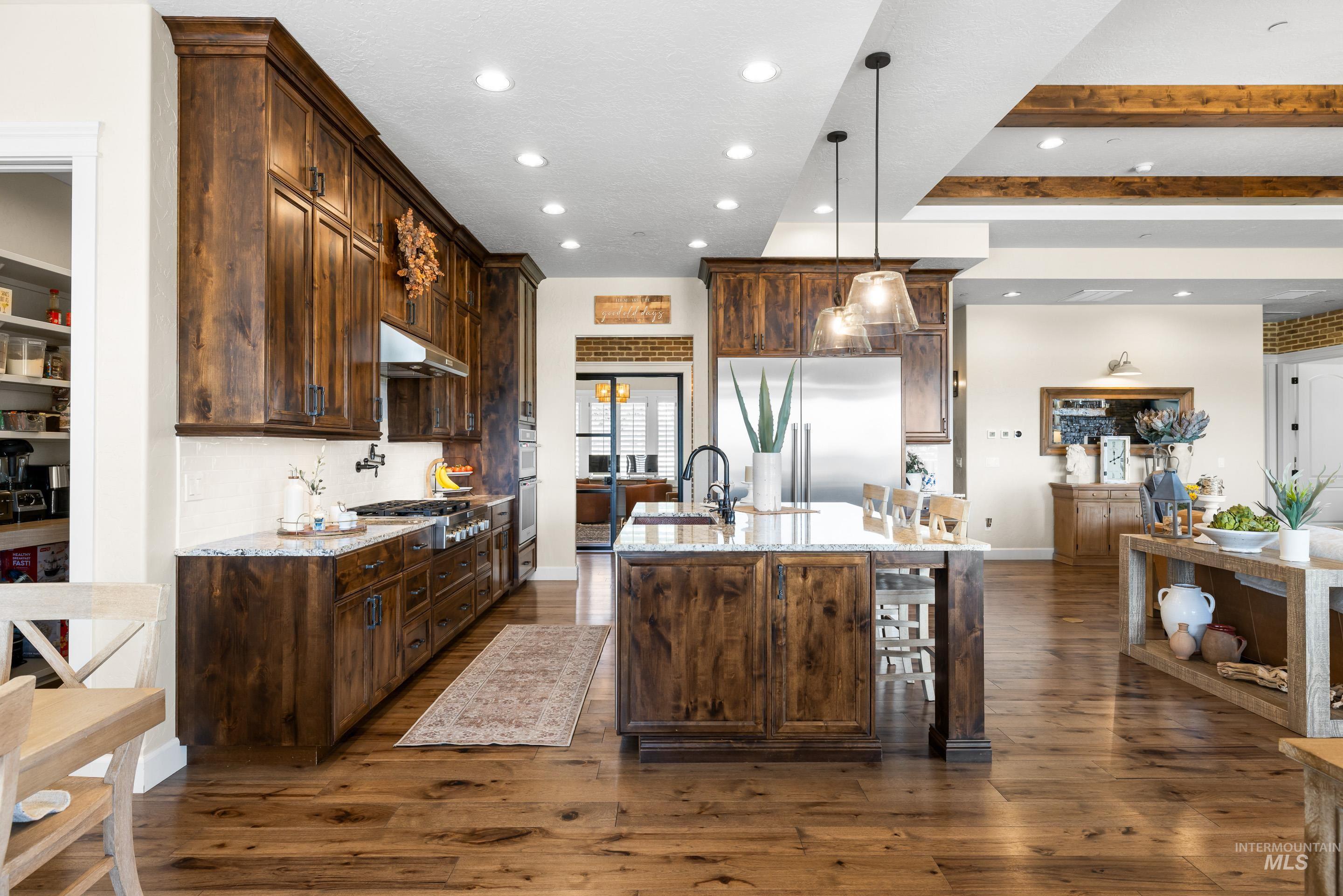 Kitchen featuring dark wood-type flooring, recessed lighting, an island with sink, dark brown cabinets, and light stone counters