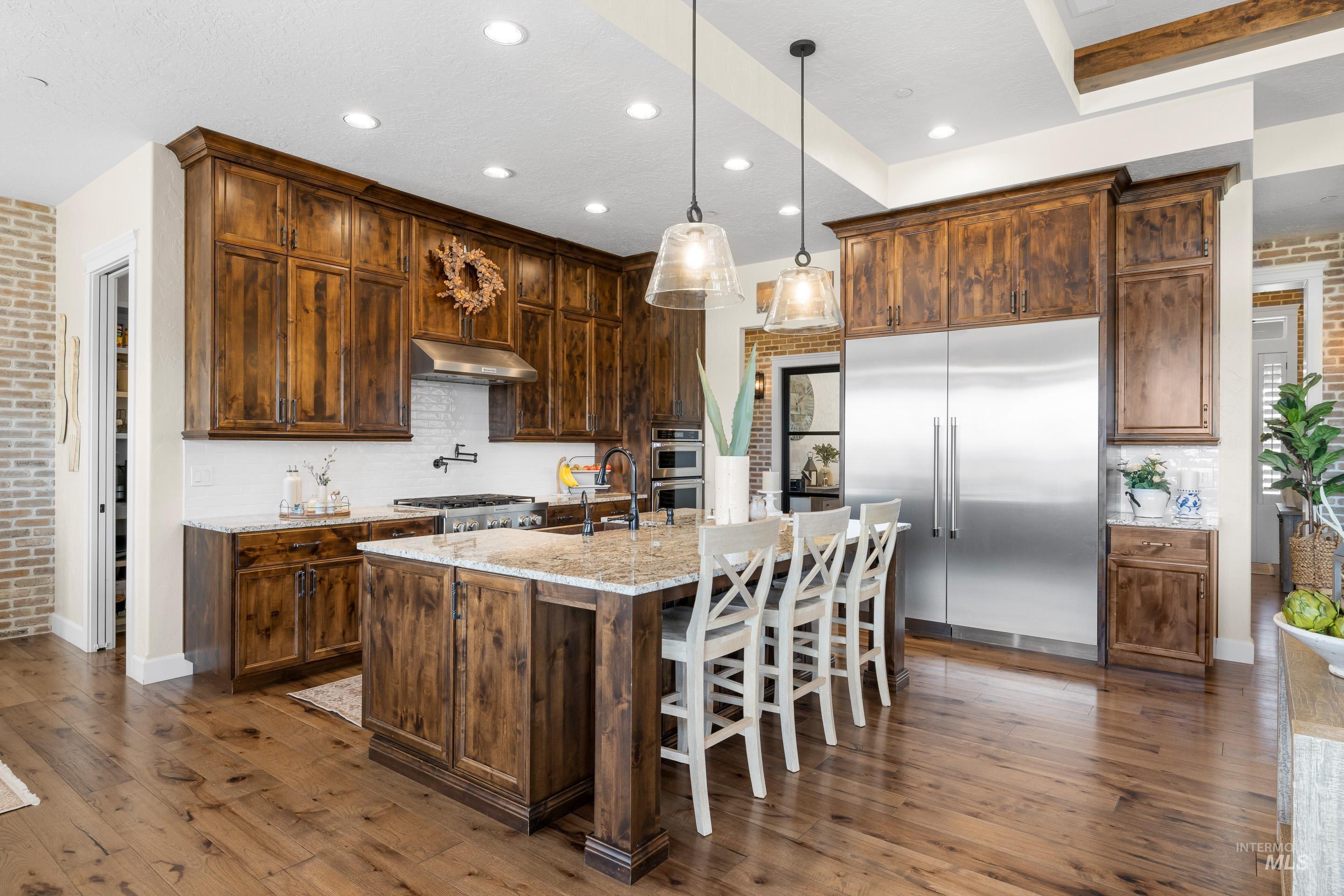 Kitchen with brick wall, appliances with stainless steel finishes, decorative backsplash, dark wood finished floors, and light stone counters