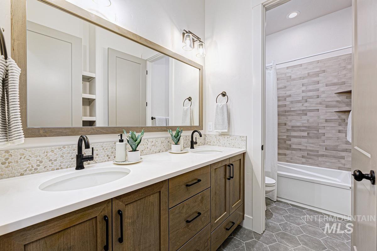 Bathroom featuring shower / bath combination with curtain, double vanity, and dark tile patterned flooring