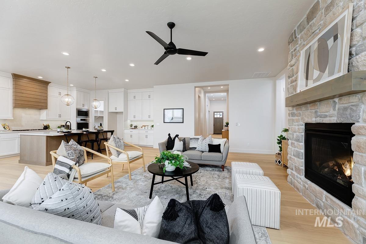 Living room featuring light wood-style flooring, ceiling fan, recessed lighting, and a stone fireplace