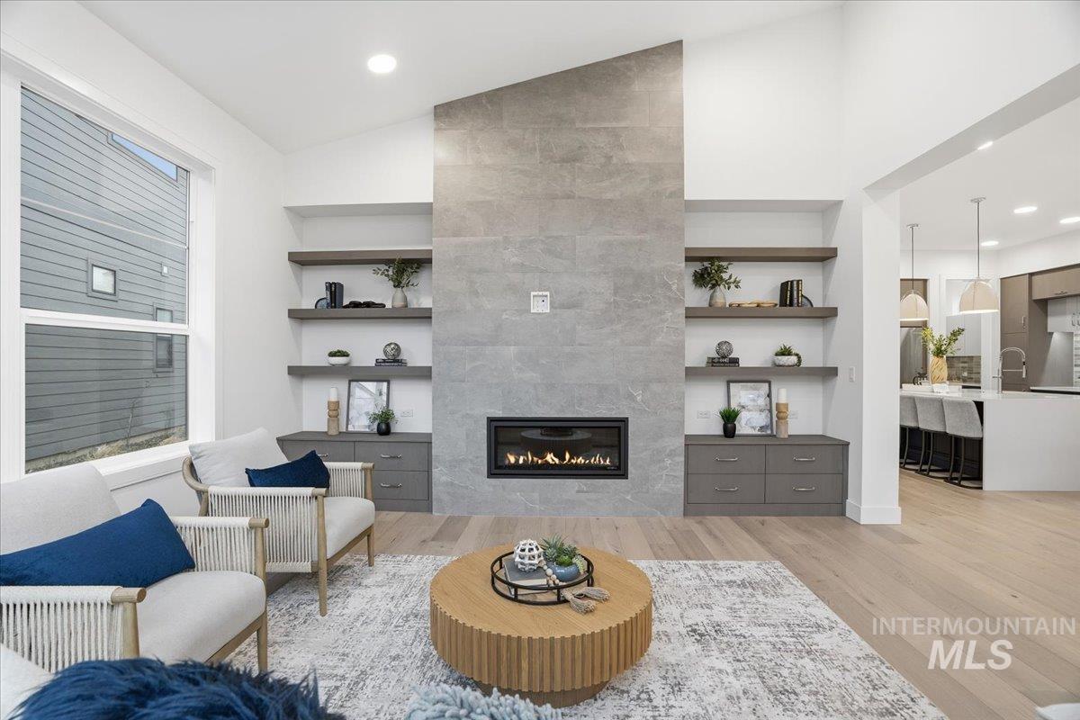 Living room with built in shelves, vaulted ceiling, a fireplace, light wood-type flooring, and radiator