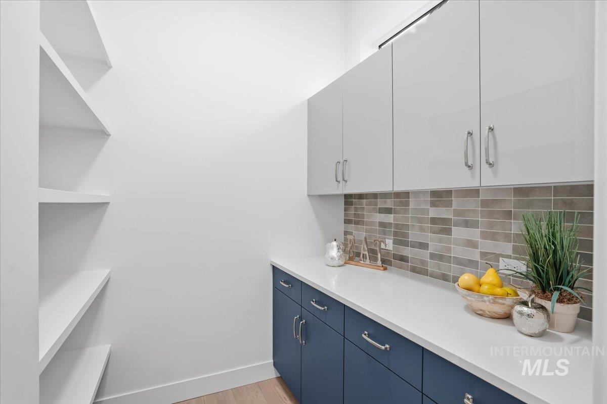 Bar featuring tasteful backsplash, blue cabinets, light wood-type flooring, and white cabinetry