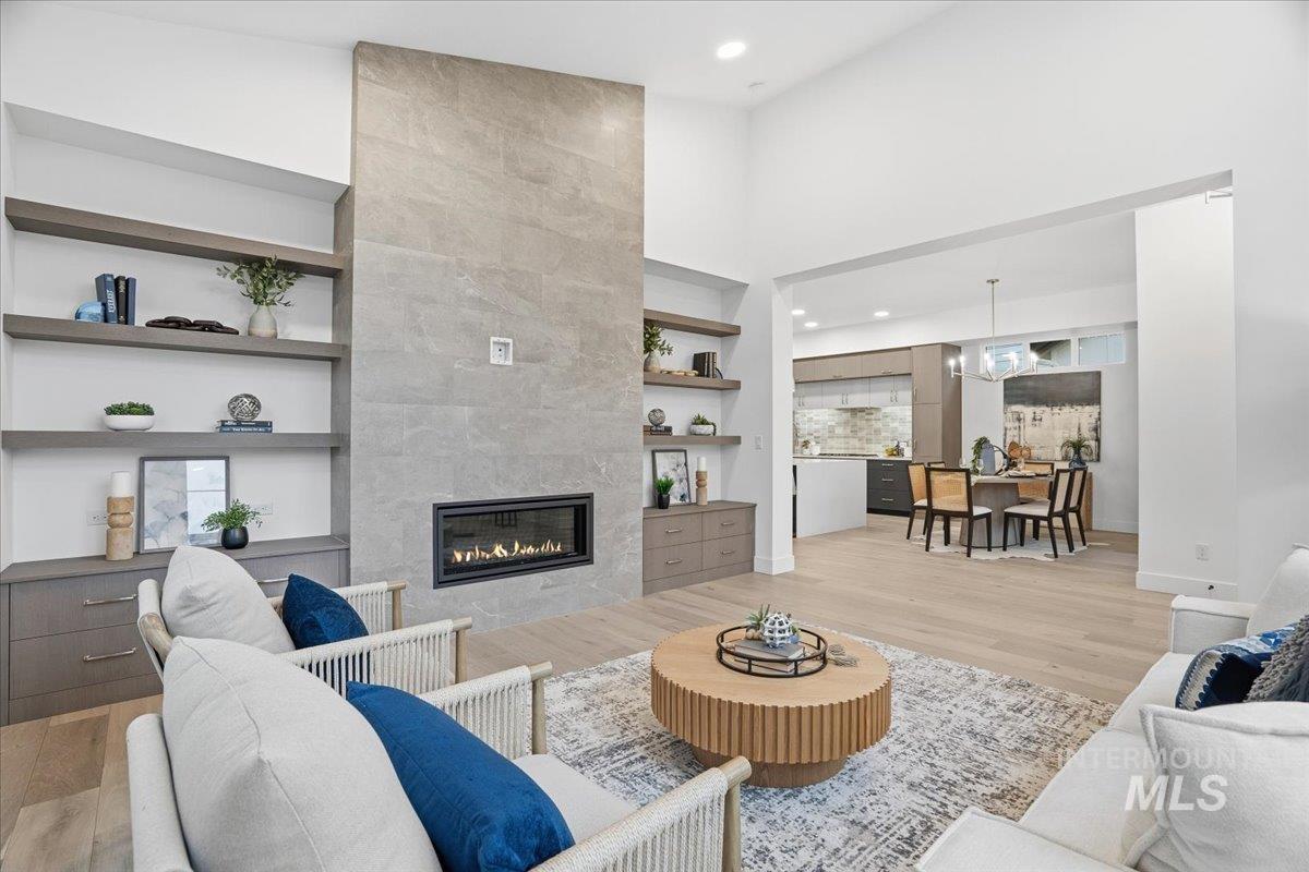 Living area featuring built in features, a fireplace, light wood-type flooring, a high ceiling, and recessed lighting