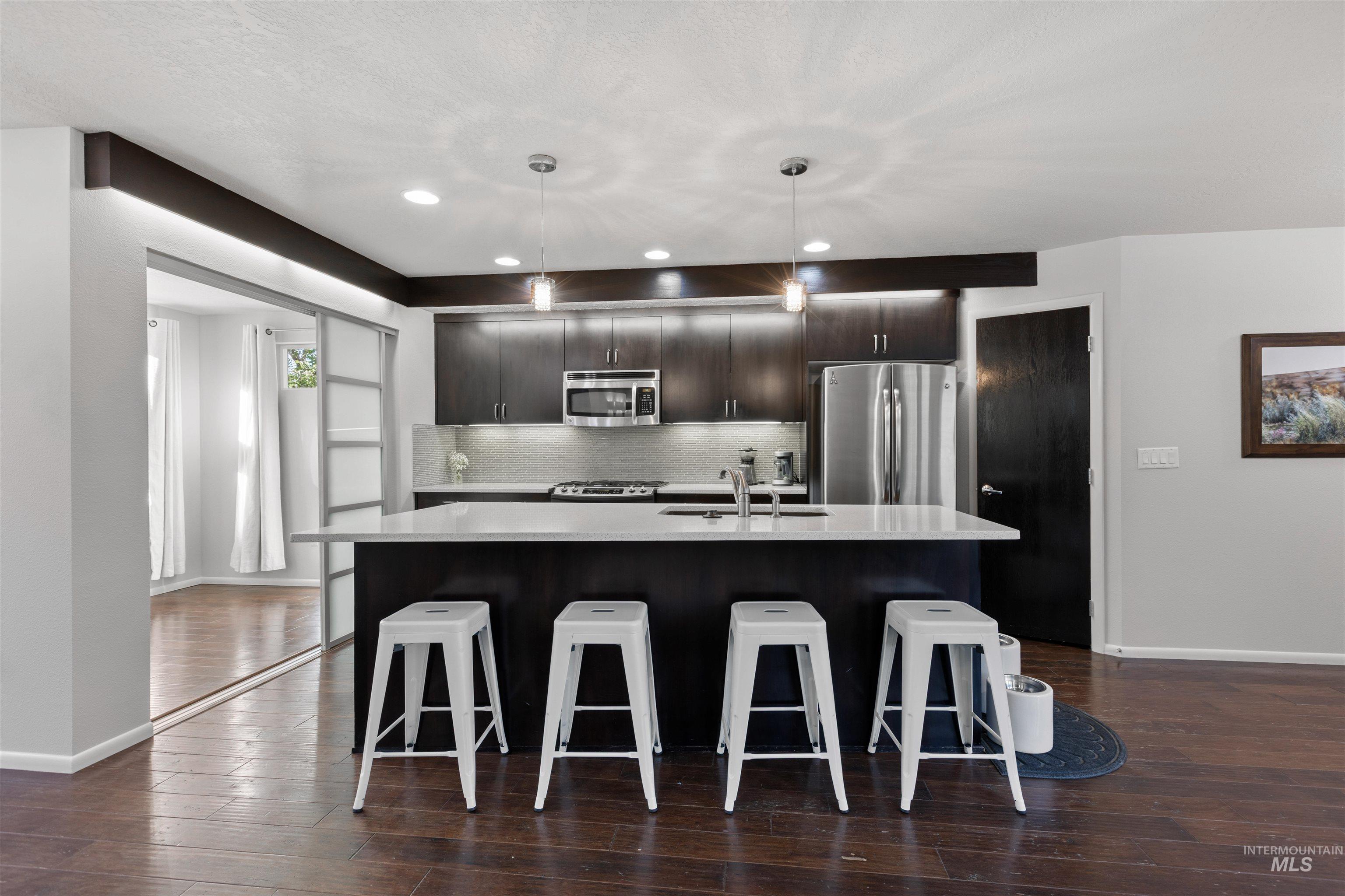 Kitchen with a breakfast bar area, dark brown cabinets, stainless steel appliances, a kitchen island with sink, and decorative backsplash